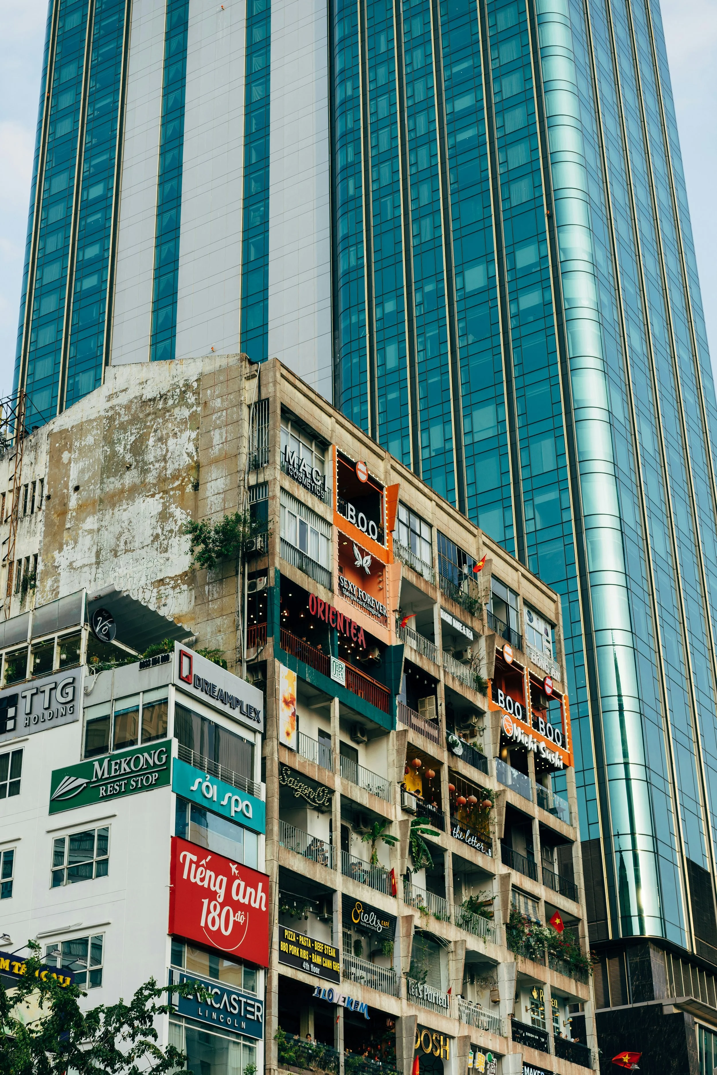 A cityscape image showing a juxtaposition of a modern glass skyscraper behind an older, weathered building with numerous signs and balconies.