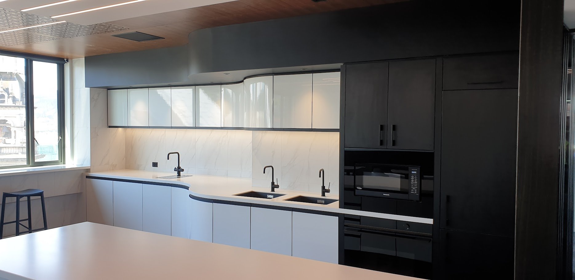 Modern kitchen with white and black cabinetry, marble backsplash, double black sink, black faucet, microwave, and natural light from large window.