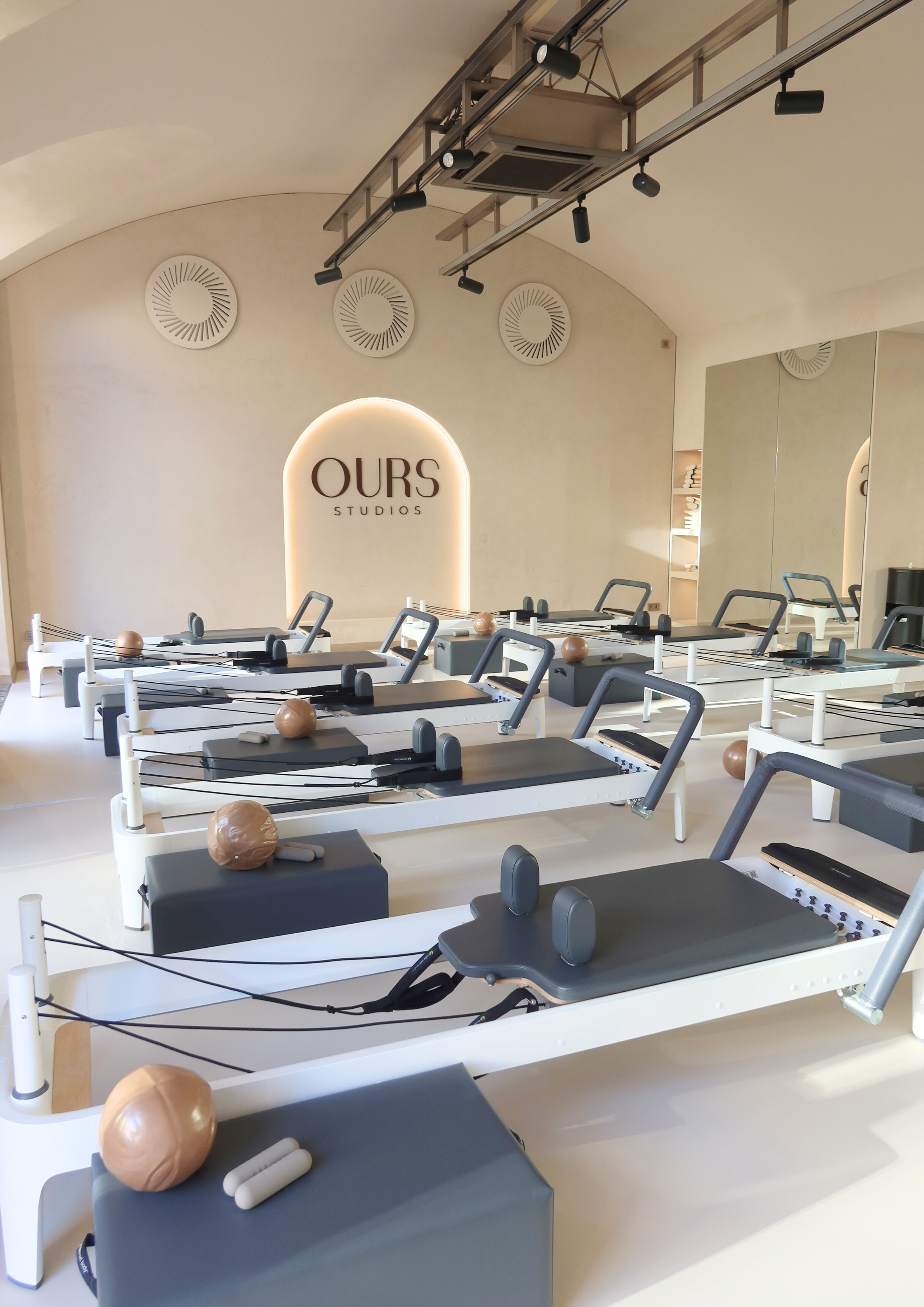 Innenraum eines Pilates-Studios mit mehreren Pilates-Geräten und dem Schriftzug 'OURS STUDIOS' an der Wand.