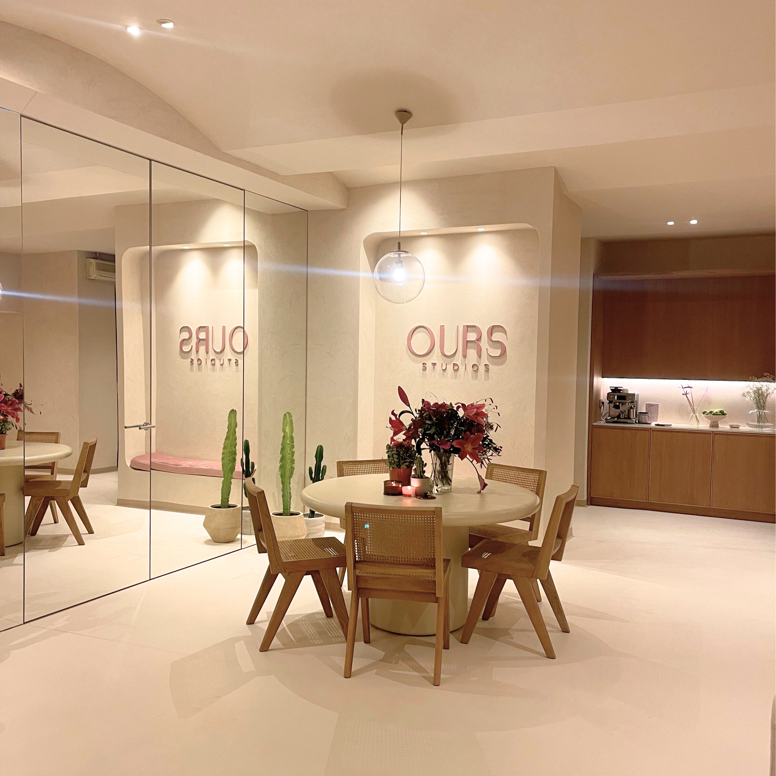 Ein modern dekorierter Raum mit einem runden Tisch, Blumen und Kerzen, einem großen Spiegel und einer Küchenzeile im Hintergrund.