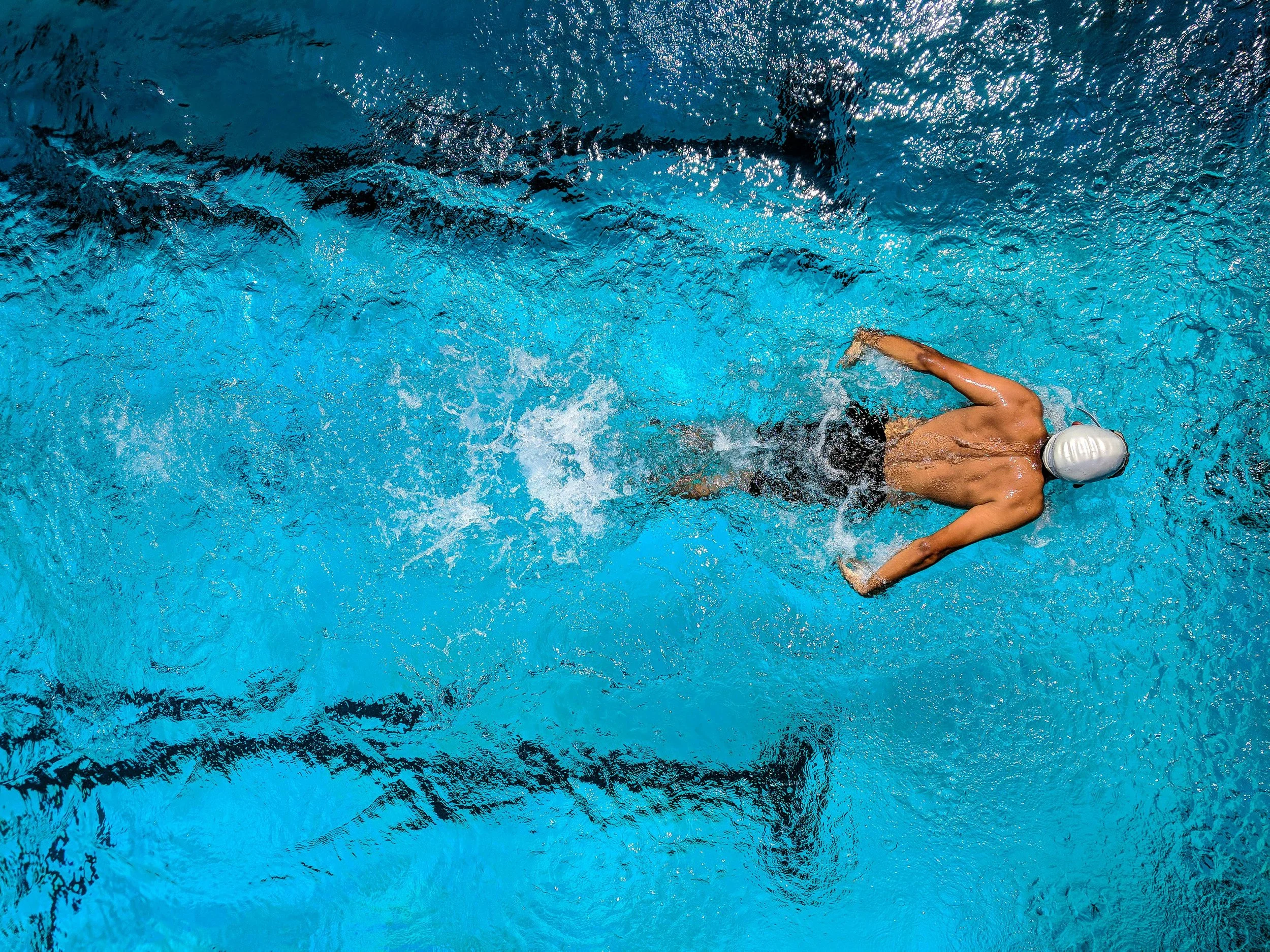 A swimmer in a white cap swimming freestyle in a blue pool.