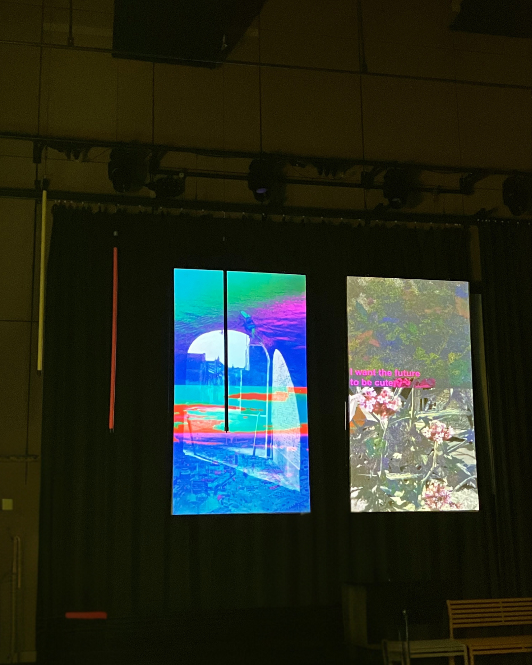 Two vertical digital screens display colorful images; the left screen shows a distorted cityscape with a large white orb and water reflection, and the right screen shows a floral pattern with pink text that reads, "I want the future to be cute."