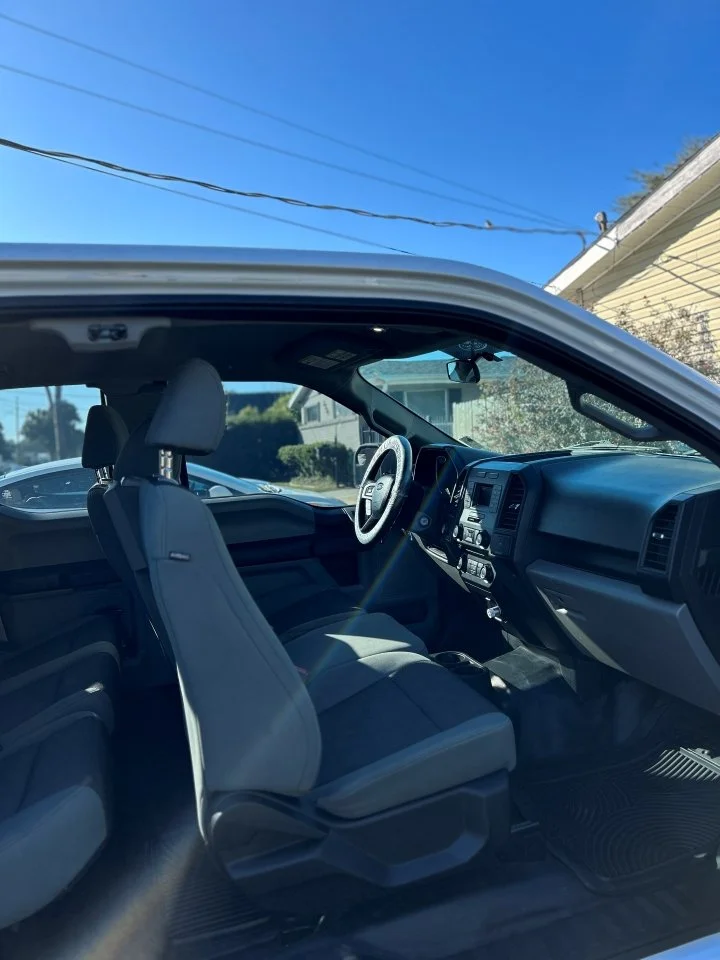 The interior of a vehicle with front seats, steering wheel, dashboard, and a glimpse of the outside residential neighborhood through the windshield in Kenner after an interior Detail | Pro Purple Mobile Detailing