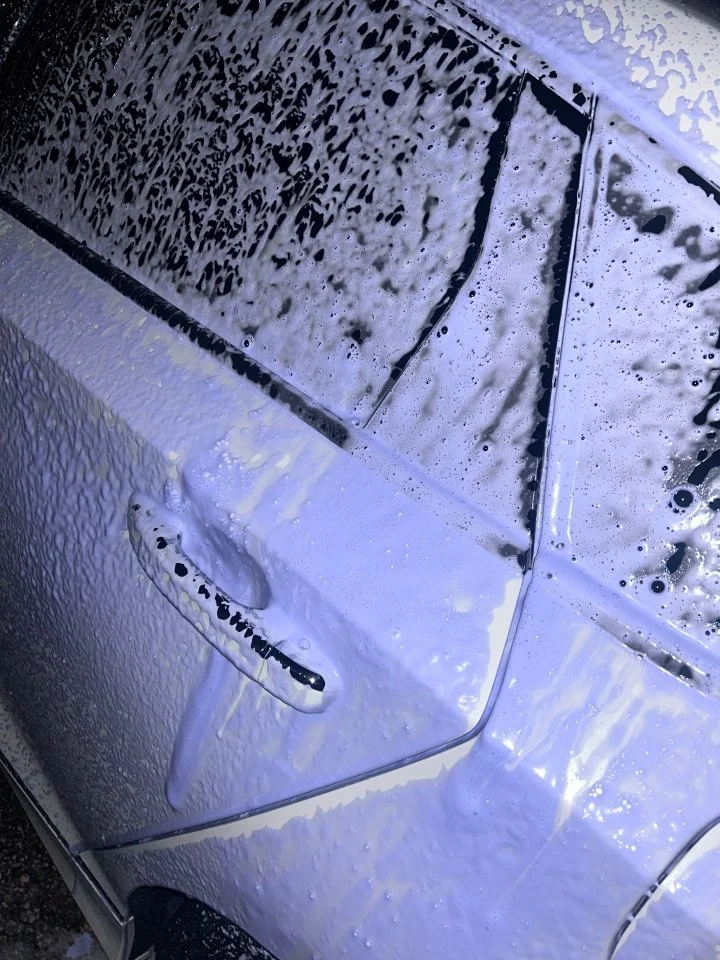 Close-up of a car's side mirror and door covered in soap suds during washing.