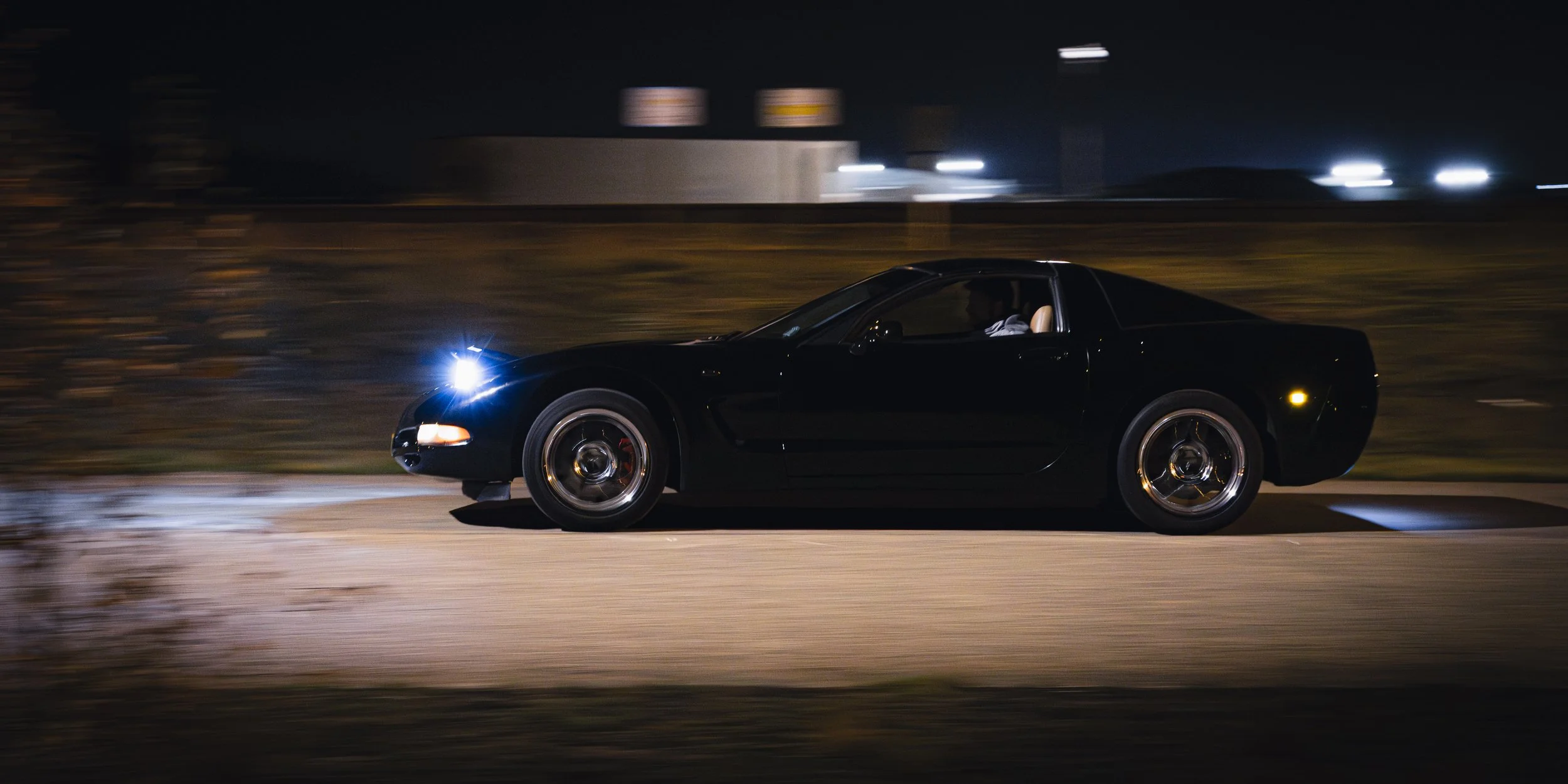 A black sports car driving at night on a street with blurred background and headlights on