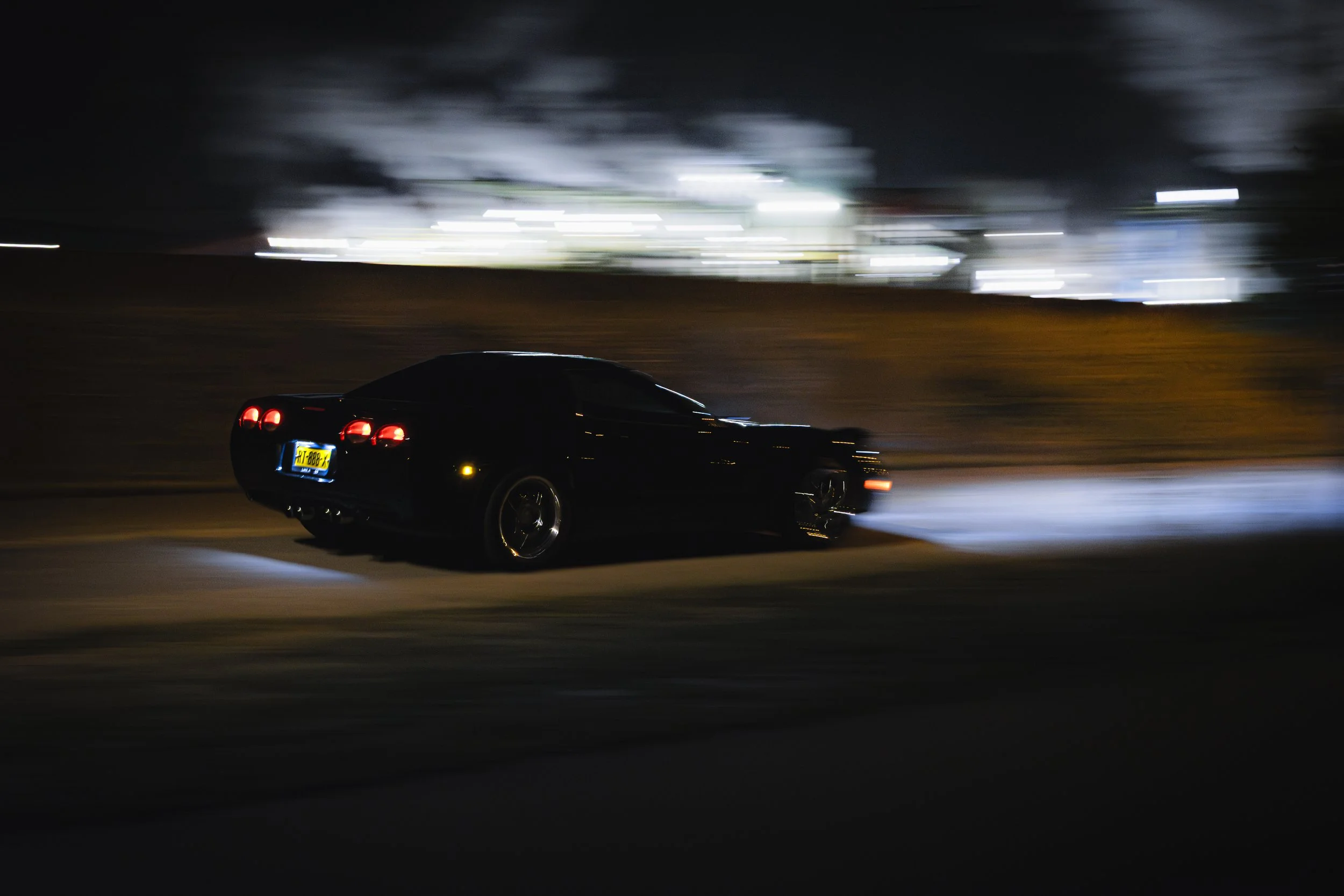 A black sports car moving at night with blurred surroundings and bright city lights in the background.