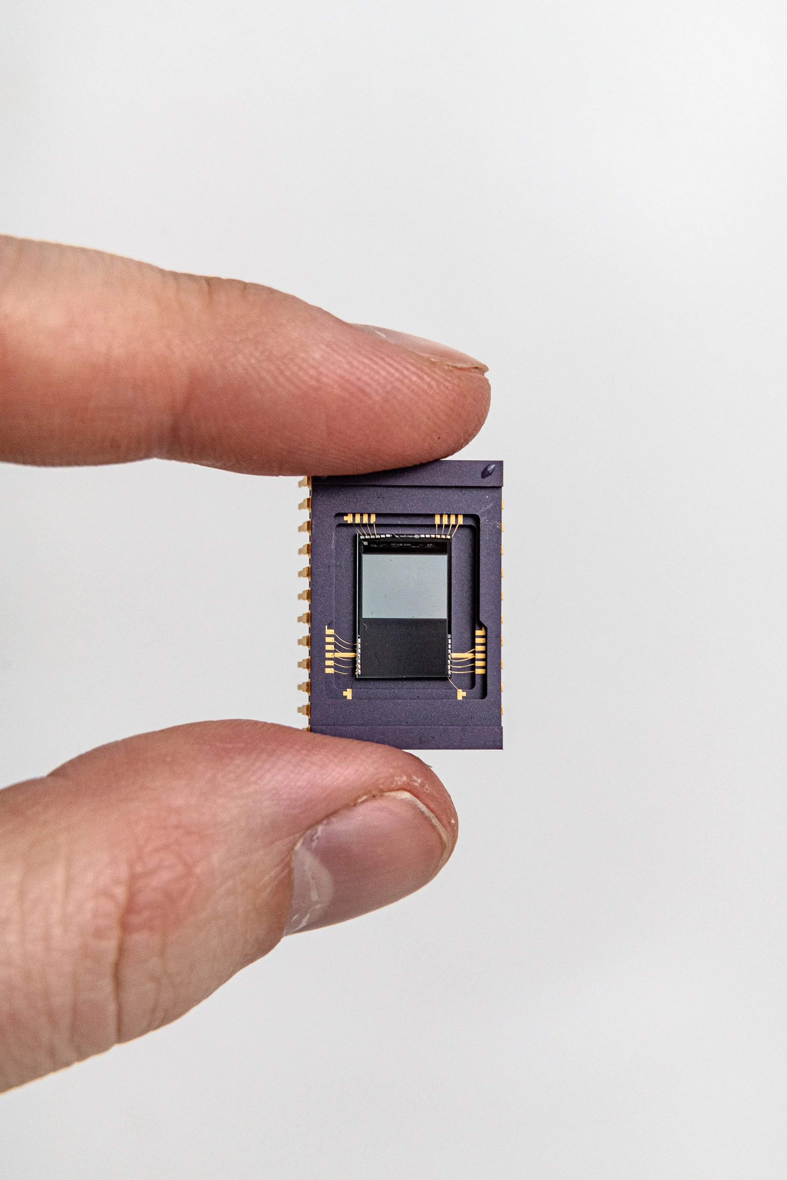 A person's fingers holding a microchip with a small camera sensor inside.