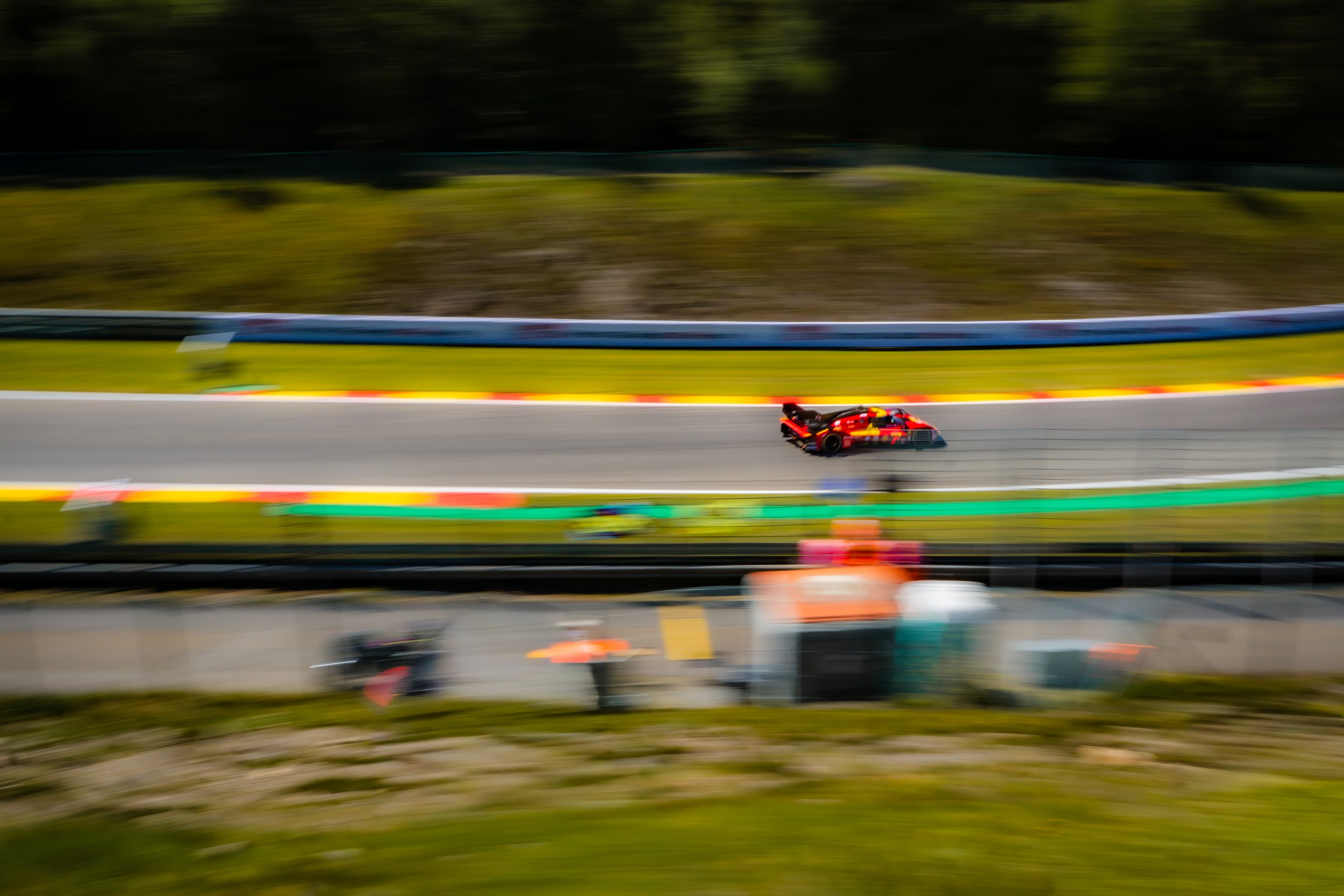 A red and black race car speeding along a racetrack, with motion blur indicating high speed and a blurred background.