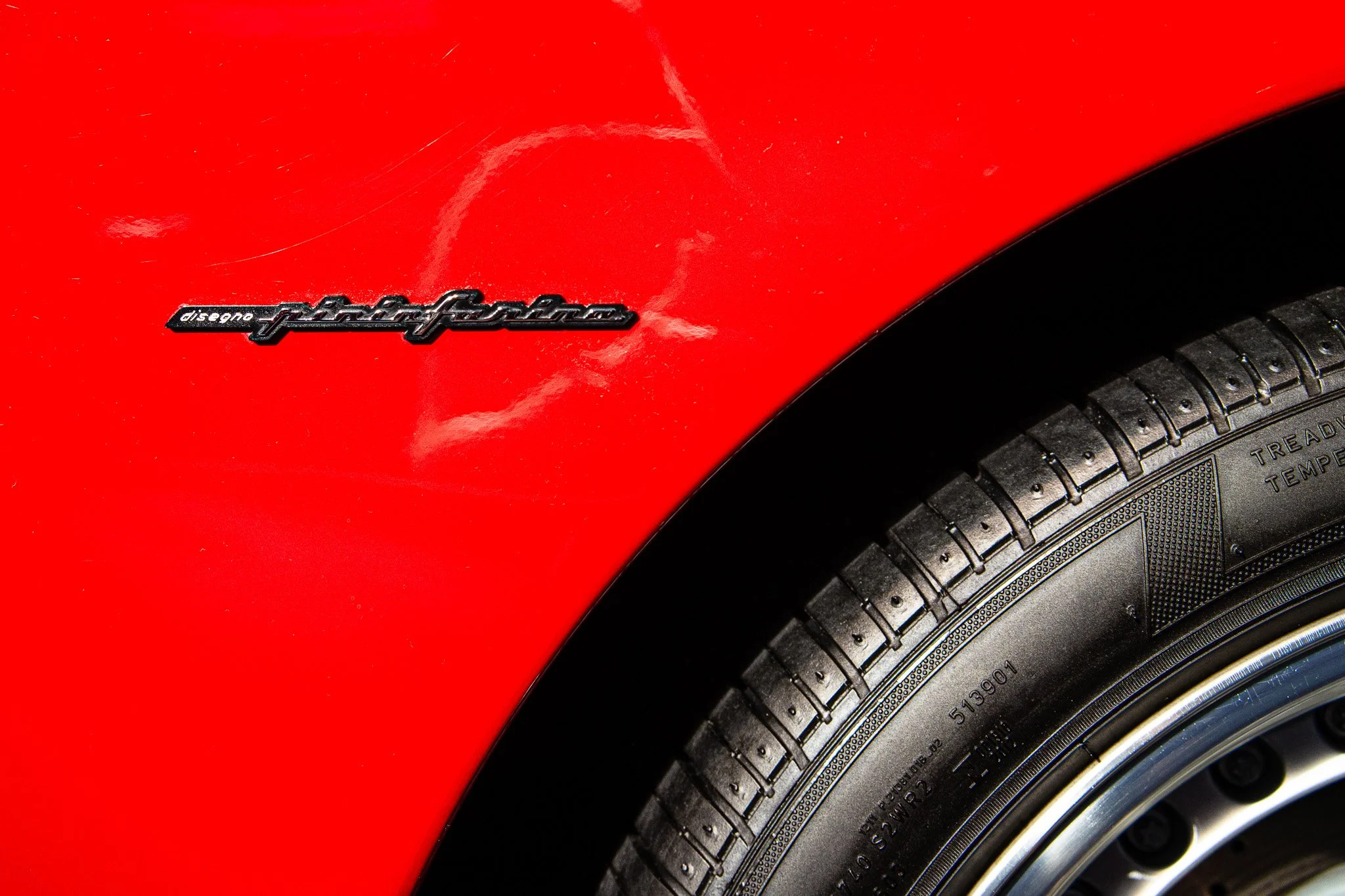 Close-up of a red Porsche car's wheel and fender with a 'Porsche' badge.