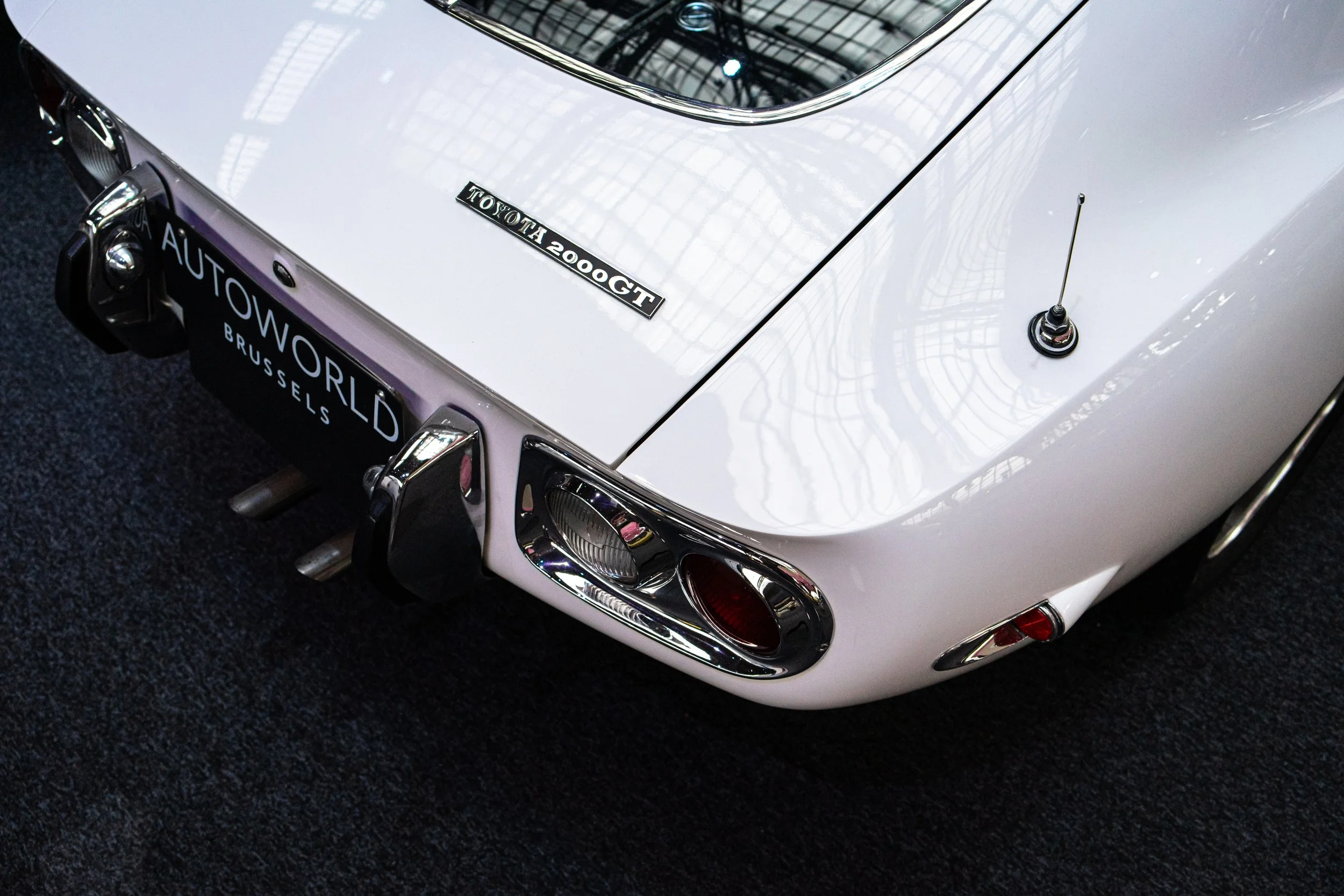 Close-up of the rear of a white vintage Toyota 2000 GT sports car showing taillights, bumper, and model badge.