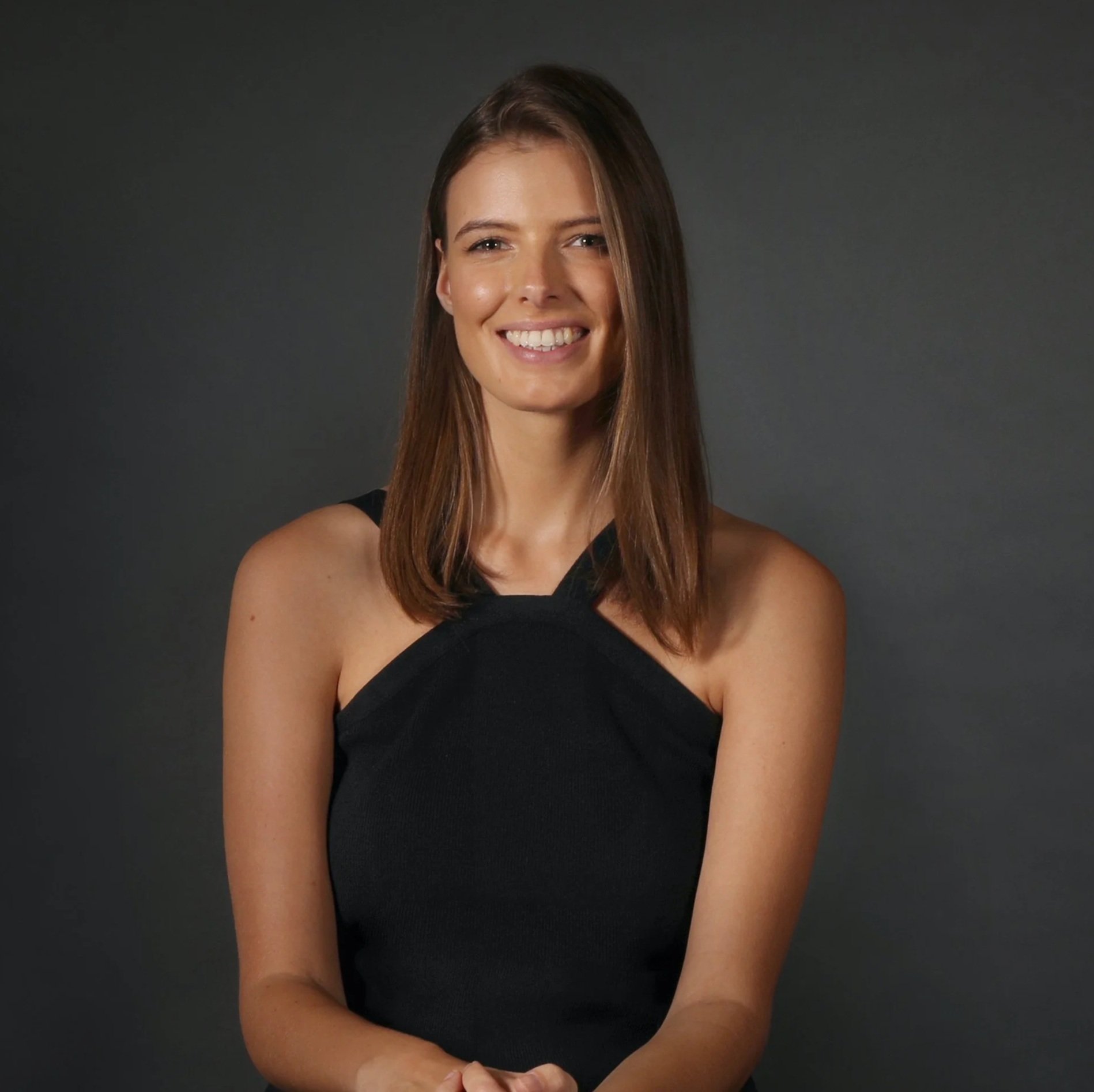 Mimi Seagar, brand and graphic designer, A young woman with shoulder-length brown hair, smiling and wearing a black sleeveless top, standing against a dark gray background.
