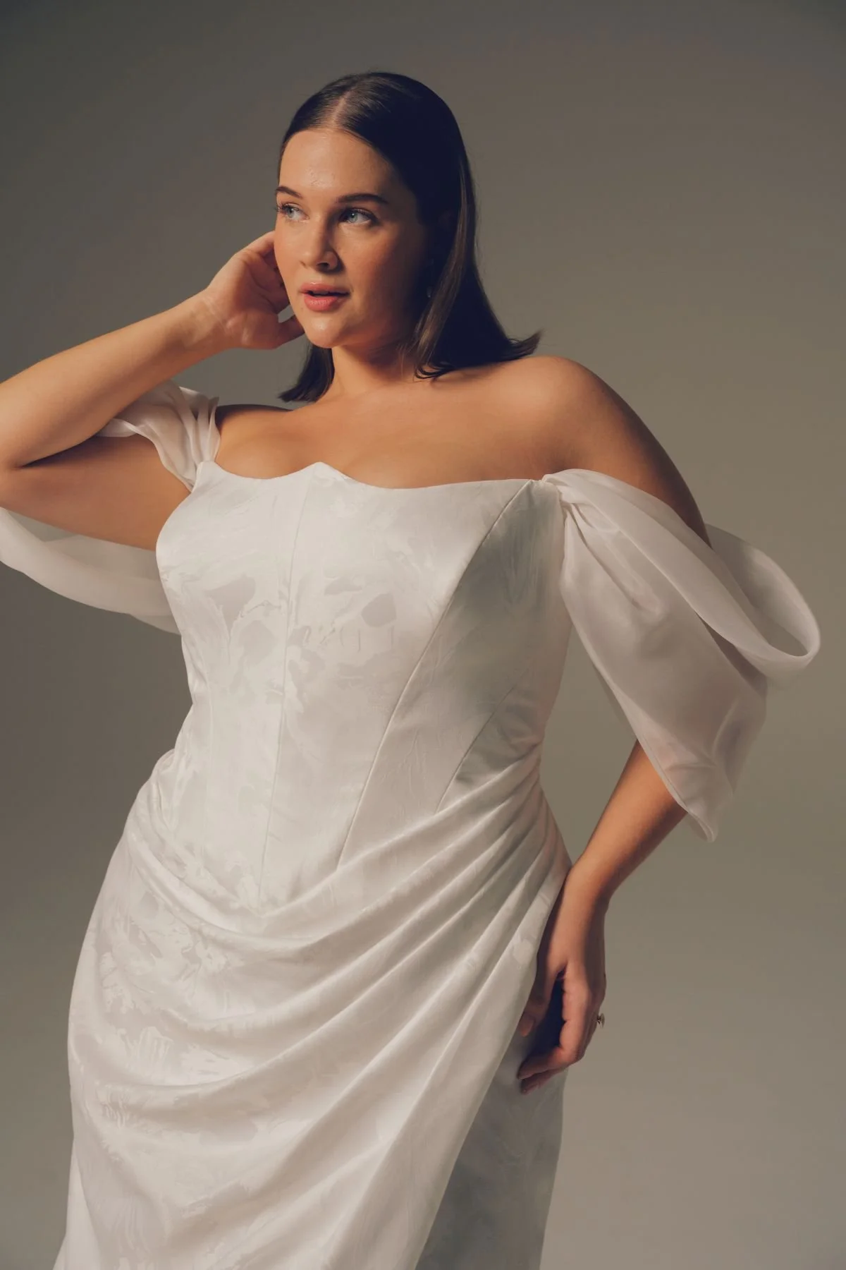 Woman with dark hair wearing a white off-shoulder dress.