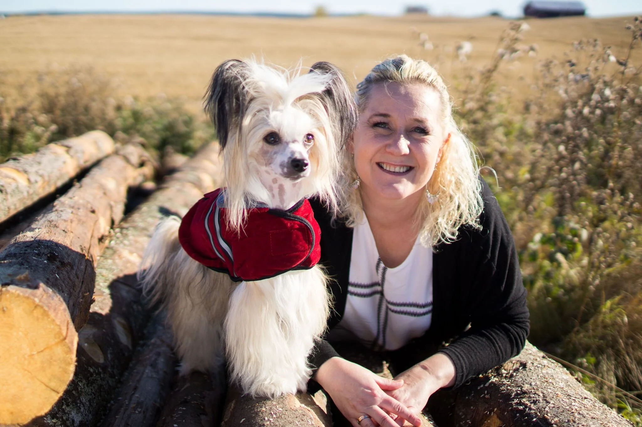 En kvinne og en hund som sitter på trær og smiler utendørs.