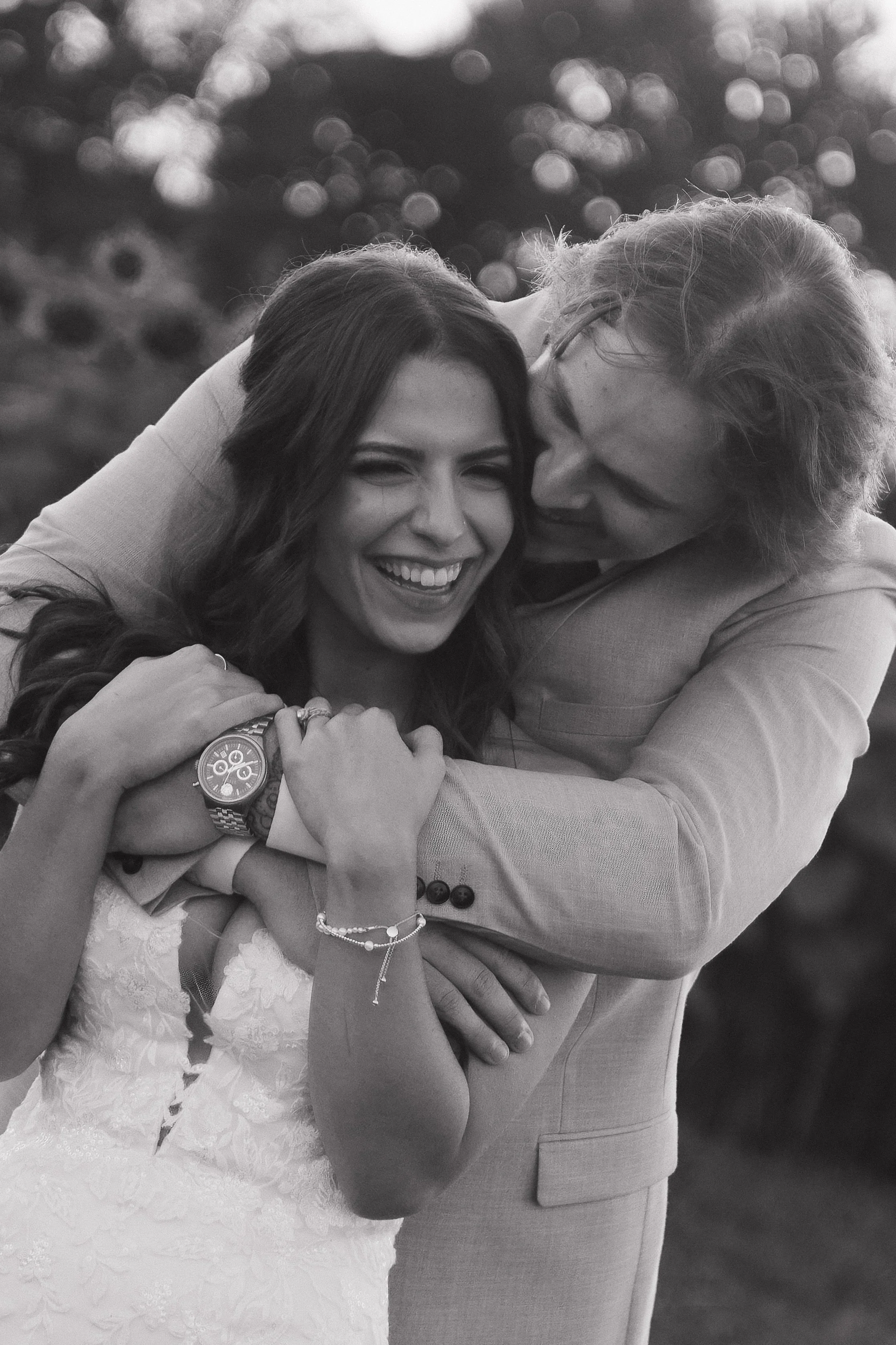 Groom hugging the bride from behind as they laugh together on their Ontario wedding day, photographed by James and Alyson Photo