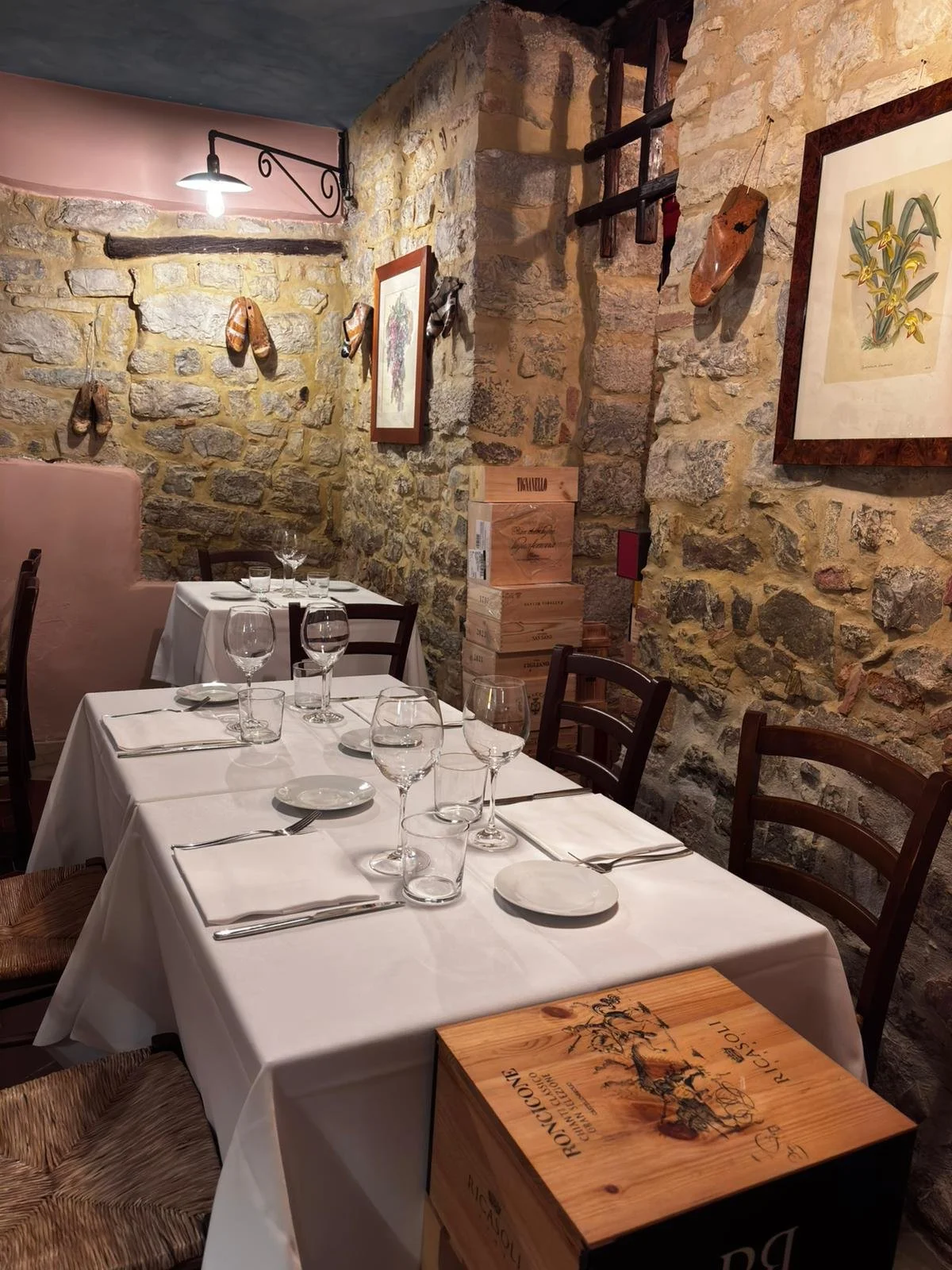A cozy restaurant corner with a stone wall, wooden chairs, and a table set modern place settings makes for a perfect meal in Tuscany. Located in the 'restaurant village' of Villa A Sesta, Castelnuovo Berardenga, Siena countryside.