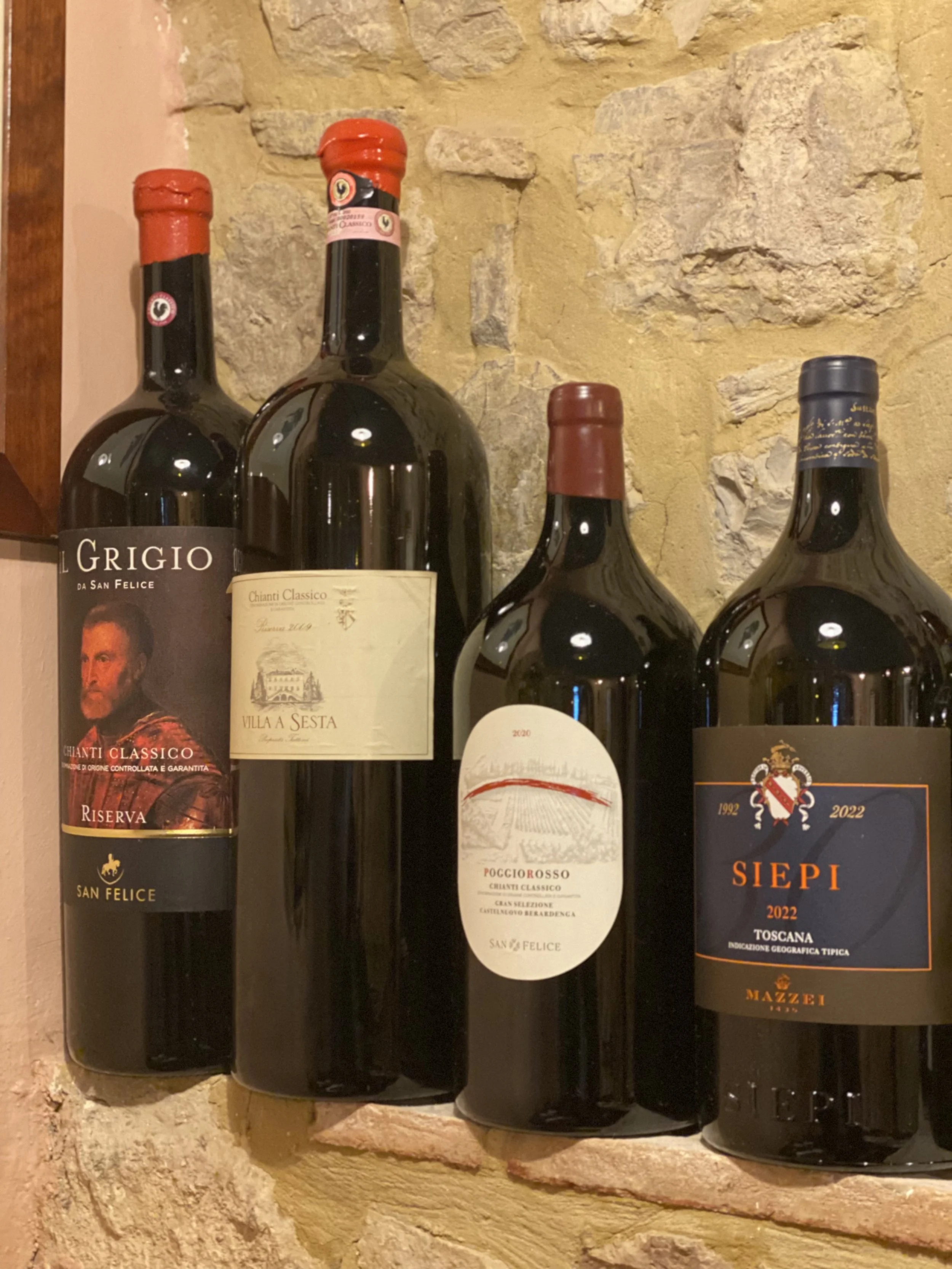 Four bottles of Italian red wine on a stone shelf against a stone wall inside Osteria Alla Villa,  a cozy restaurant with great ambiance in Tuscany, Siena, Castelnuovo Berardenga, Villa A Sesta.
