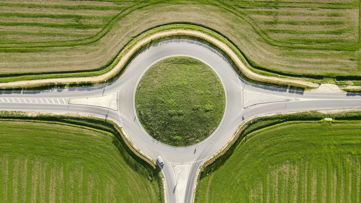 An aerial view of a circular road with a central green island surrounded by fields and farmland.