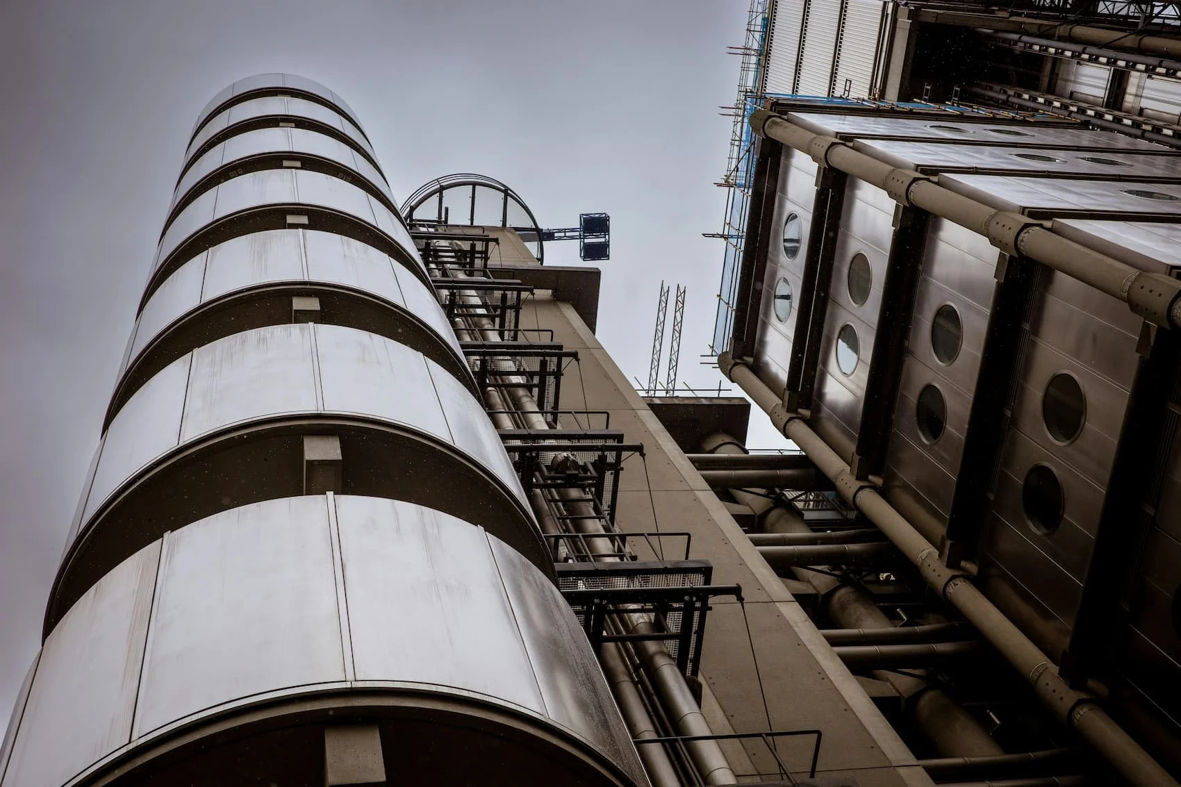 Black and white photo of tall modern buildings in a city, with one under construction or renovation, surrounded by scaffolding.