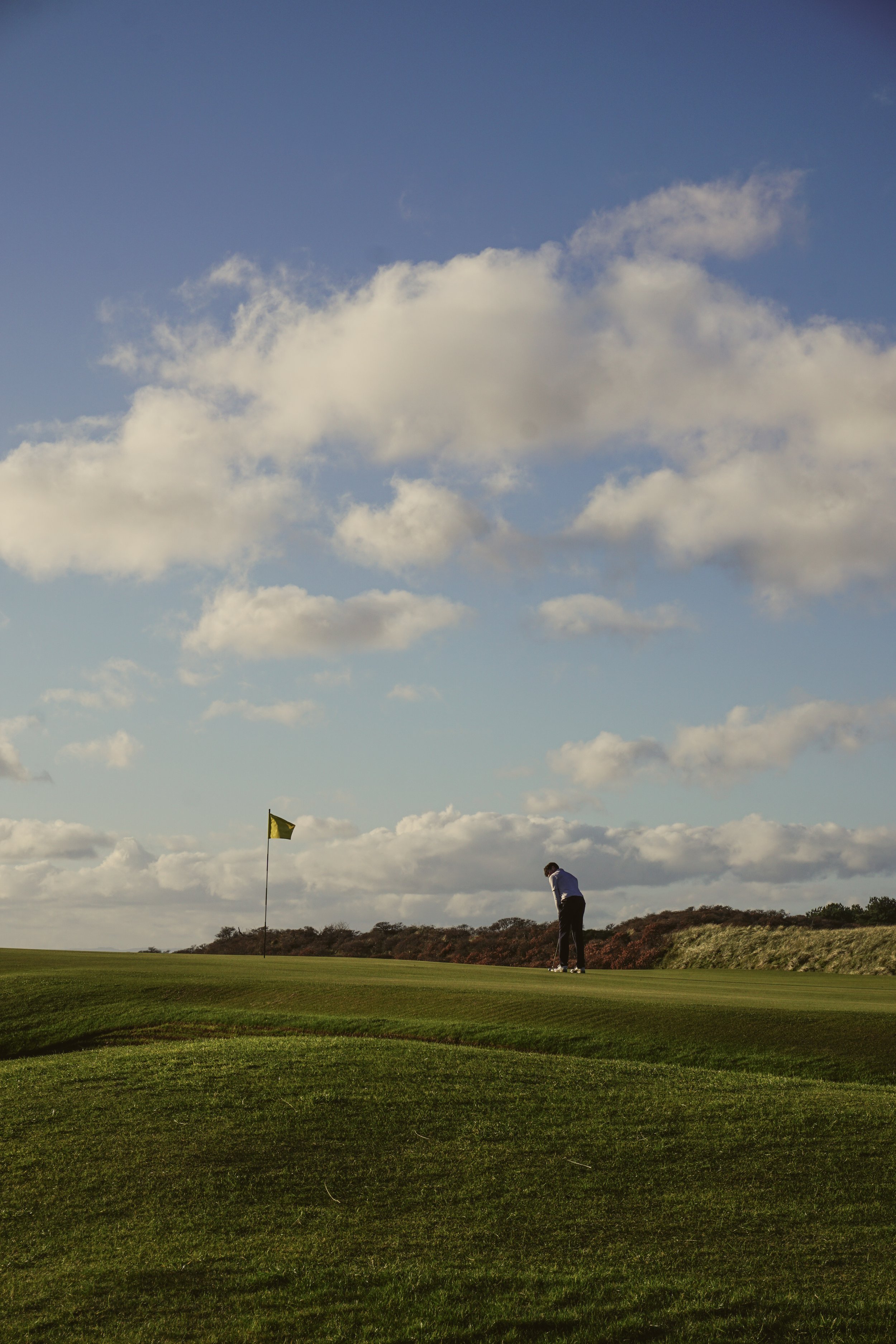 A person playing golf at muirfield near a flag on a golf course under a partly cloudy sky.