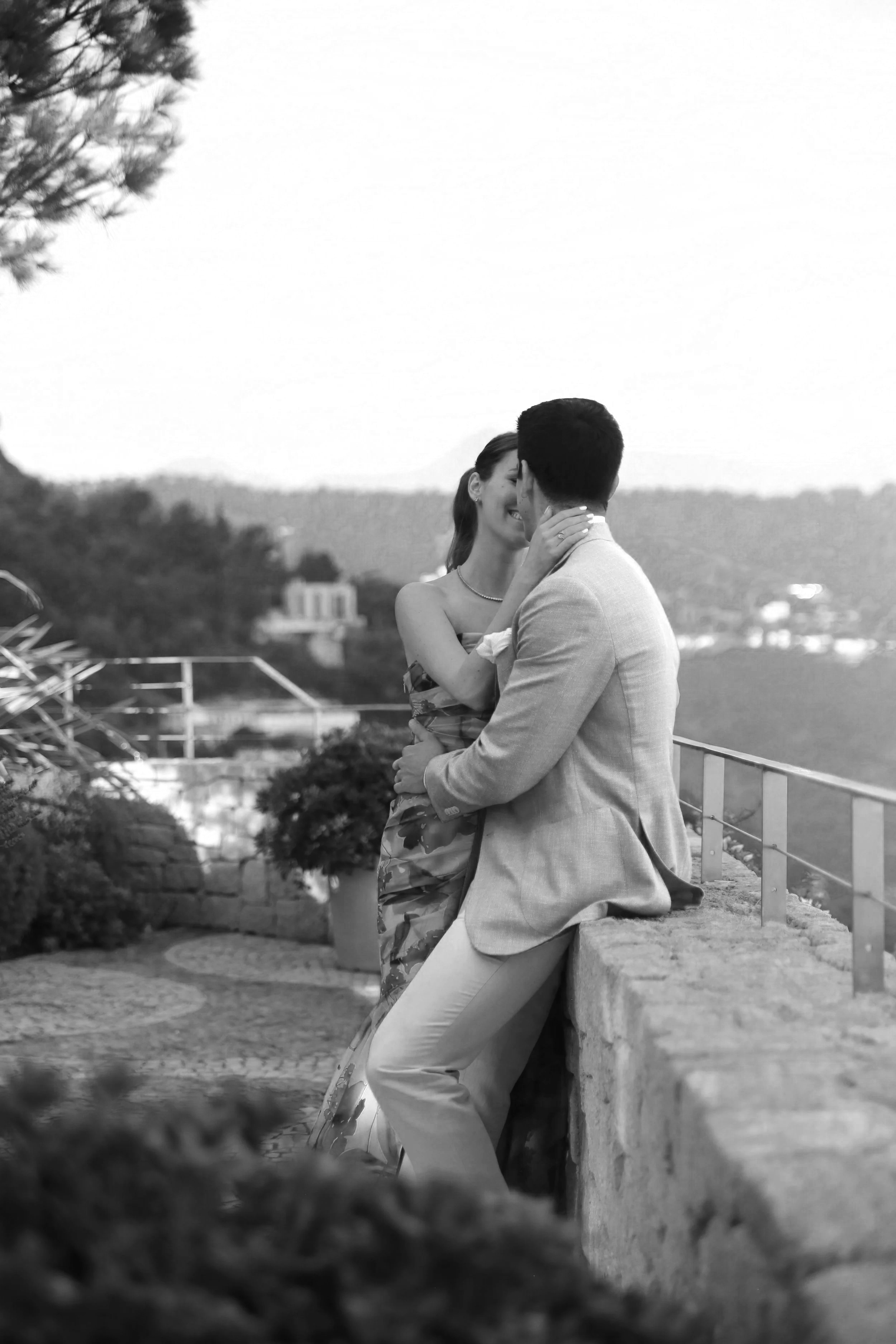 Un couple romantique en train de s'embrasser sur un balcon avec vue sur la mer, dans un style noir et blanc.