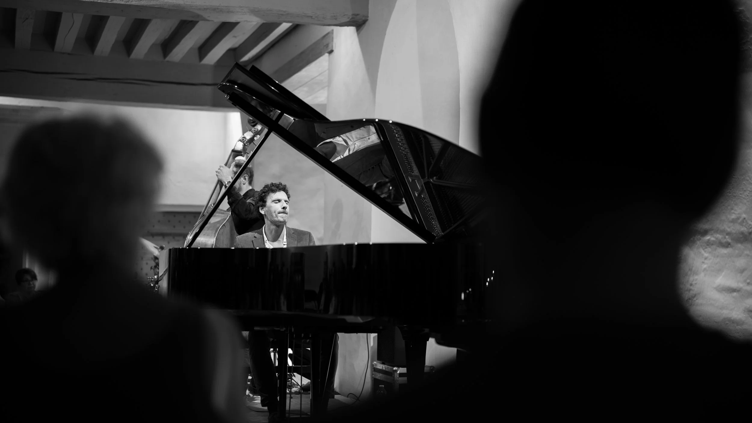 Un homme joue du piano lors d'une performance, entouré d'un public, en noir et blanc.
