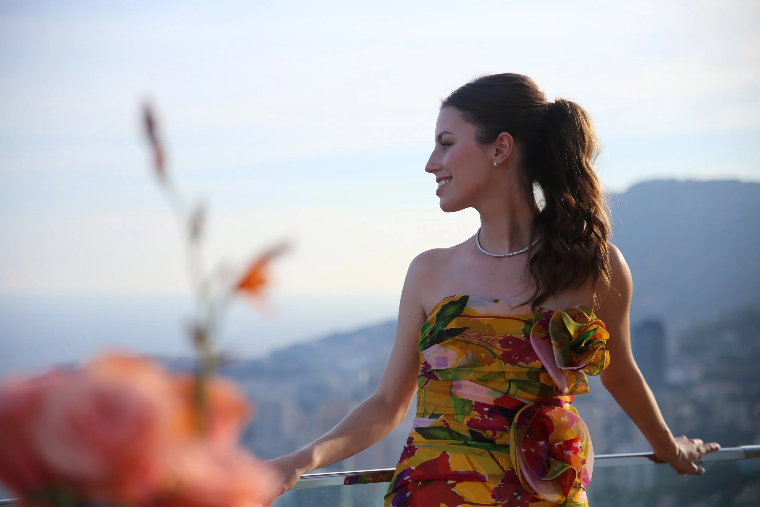 Une femme souriante portant une robe colorée, regardant vers la droite avec une vue de ville en arrière-plan