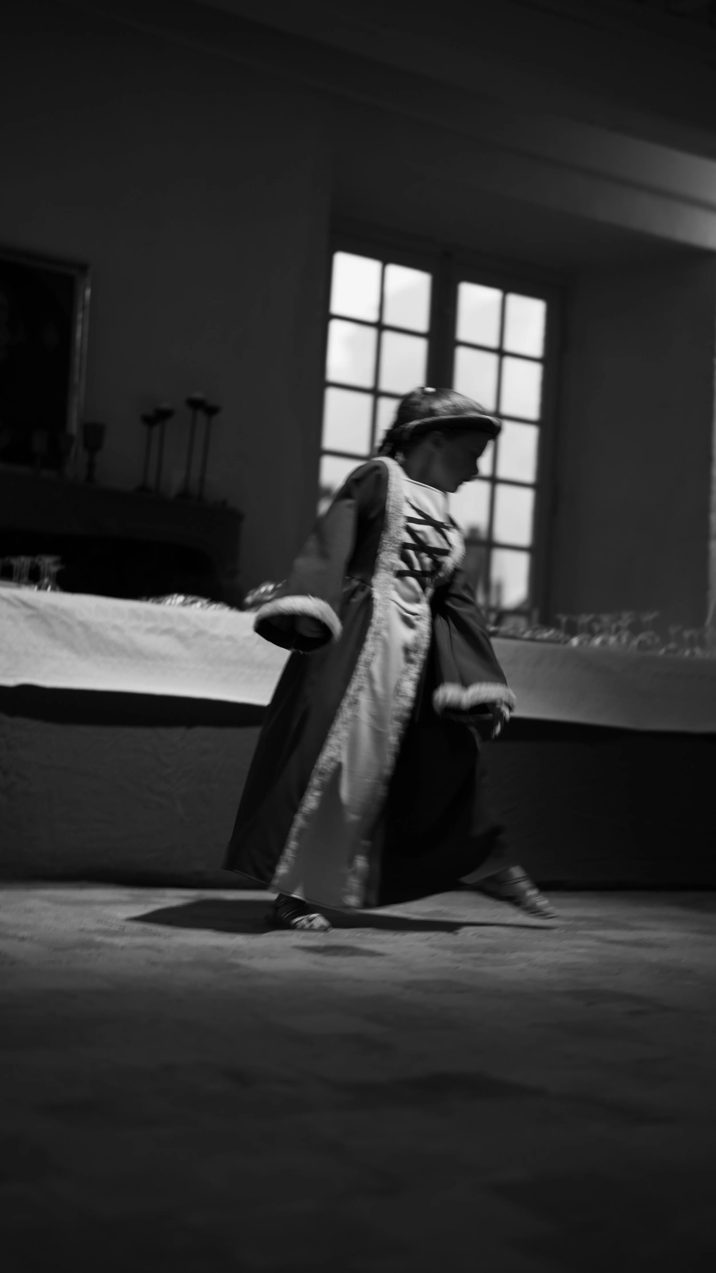 Une personne vêtue d'un costume historique, probablement pour une performance ou un spectacle, dans une pièce éclairée par une grande fenêtre.