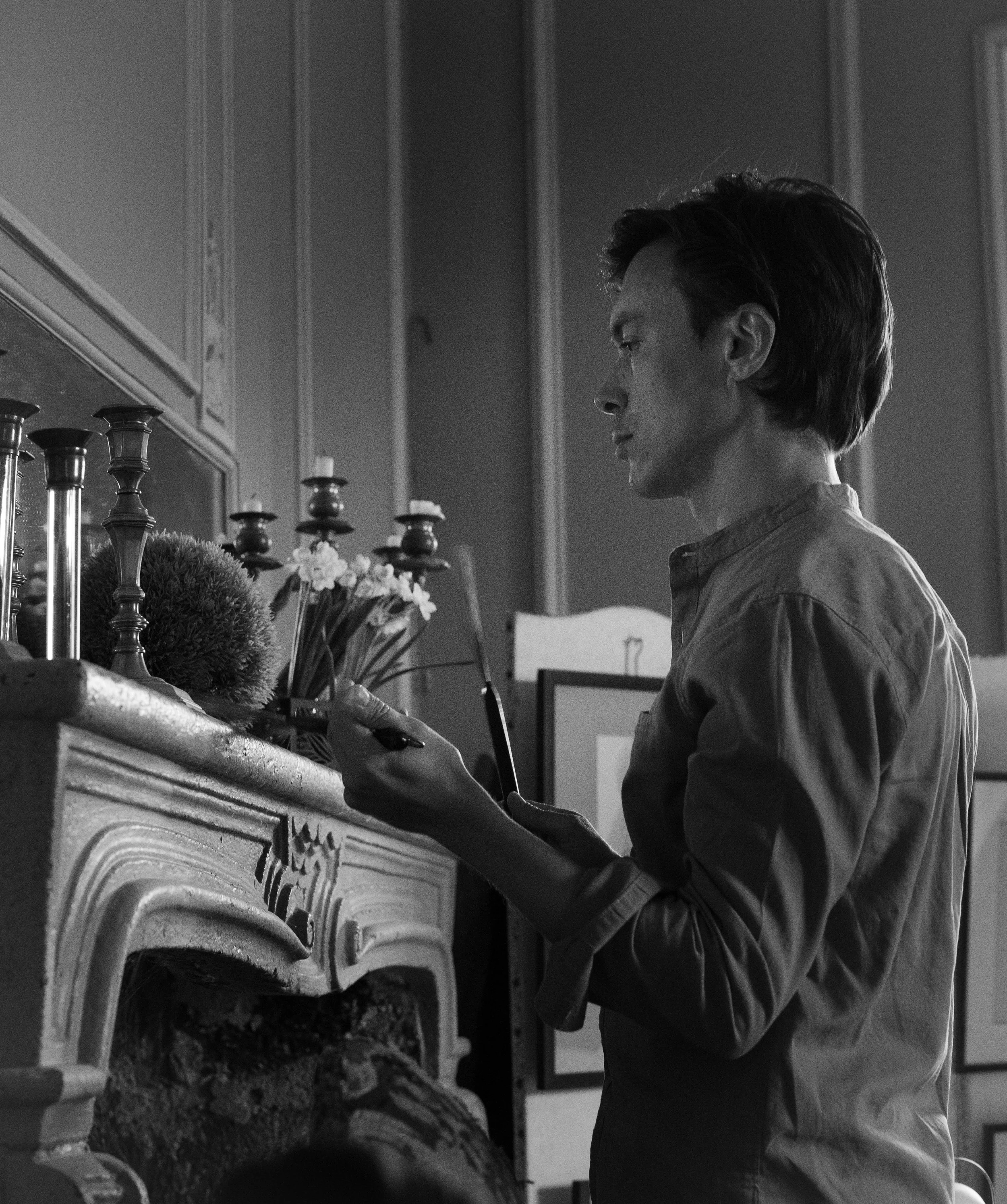 Homme regardant un smartphone devant une cheminée avec des bougies et des fleurs dans un cadre intérieur