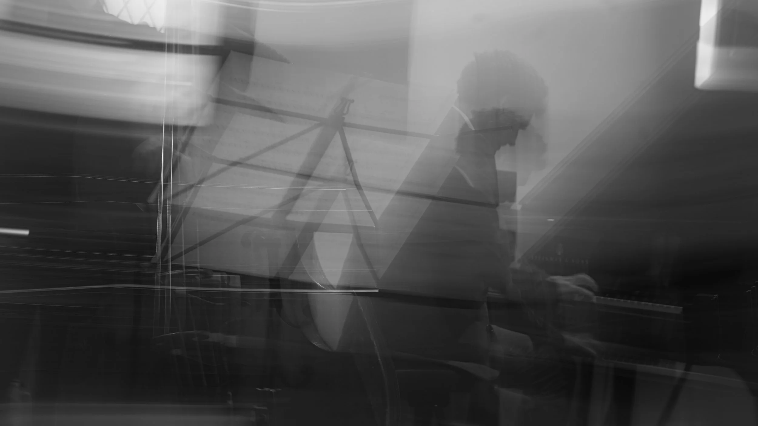 Un homme joue du piano, silhouette floue en réflexion sur une surface brillante.