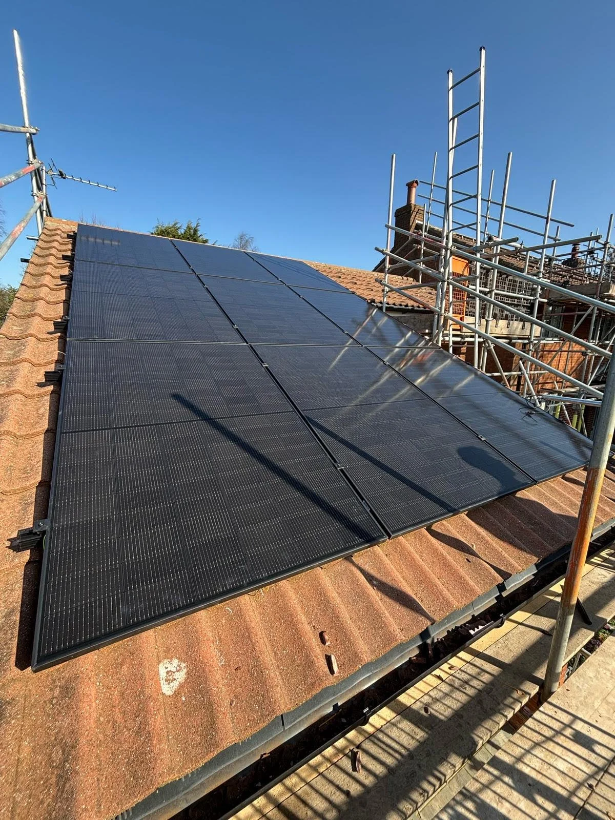 Solar panels installed on a sloped rooftop with scaffolding nearby under clear blue sky.