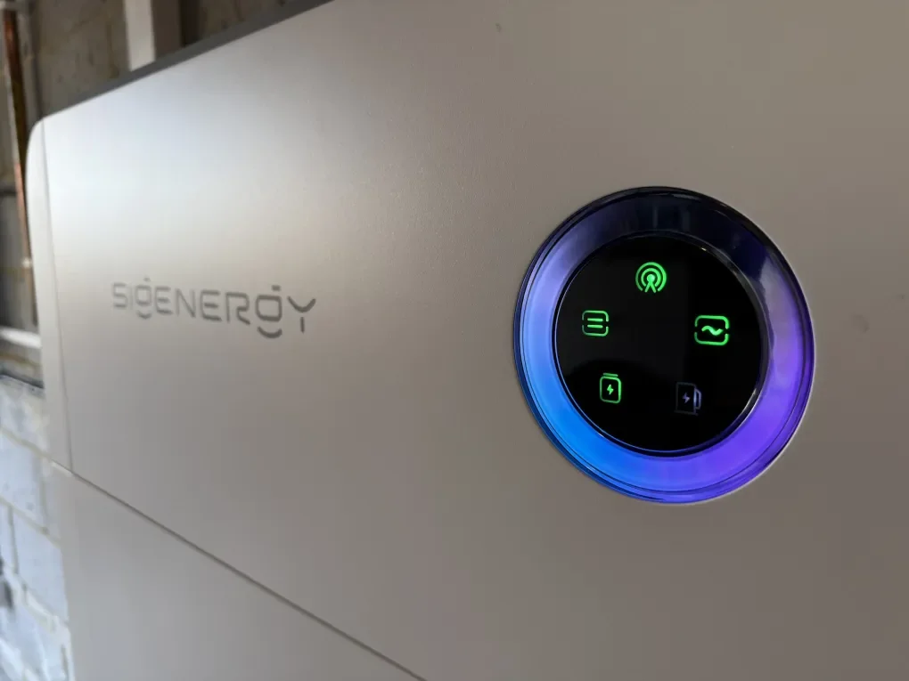 Close-up of a white energy storage system with a circular digital display showing various icons and a blue and purple LED ring.