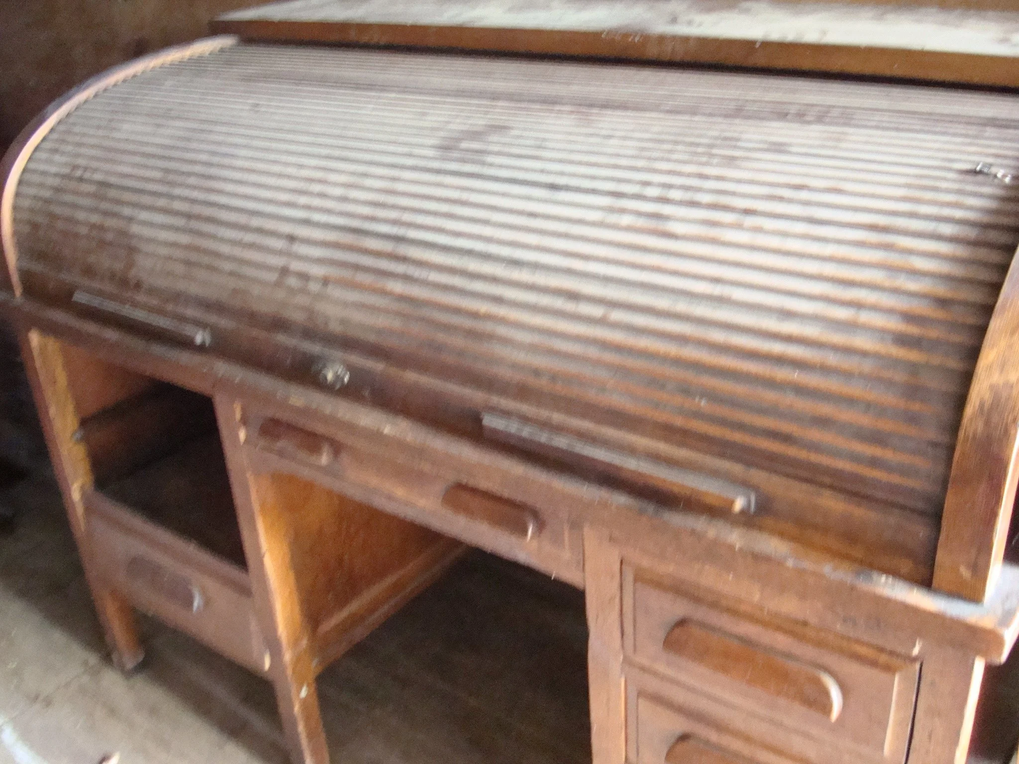 Old wooden roll-top desk with storage drawers and compartments, showing worn and aged wood.
