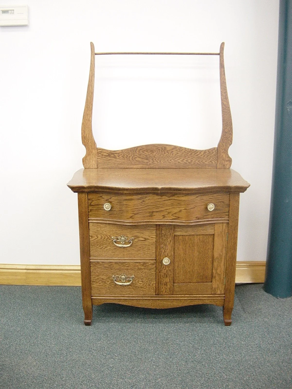 A wooden corner cabinet with small drawers and a small door, topped with a wooden frame that extends upward.