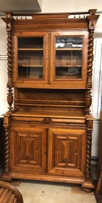 A large antique wooden cabinet with glass doors on the upper section, a middle shelf, and closed storage with two doors on the bottom.