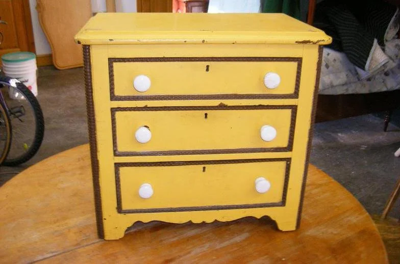Yellow vintage dresser with three drawers, white knobs, and dark trim, sitting on a wooden table.