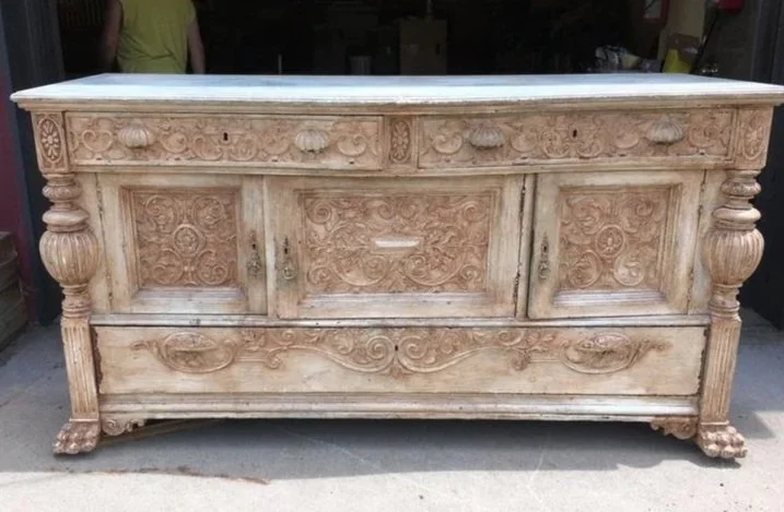An antique wooden sideboard with ornate carvings, turned legs, and a marble top.