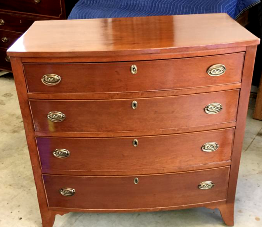 Wooden dresser with four drawers and brass handles, placed in a room with concrete floor.