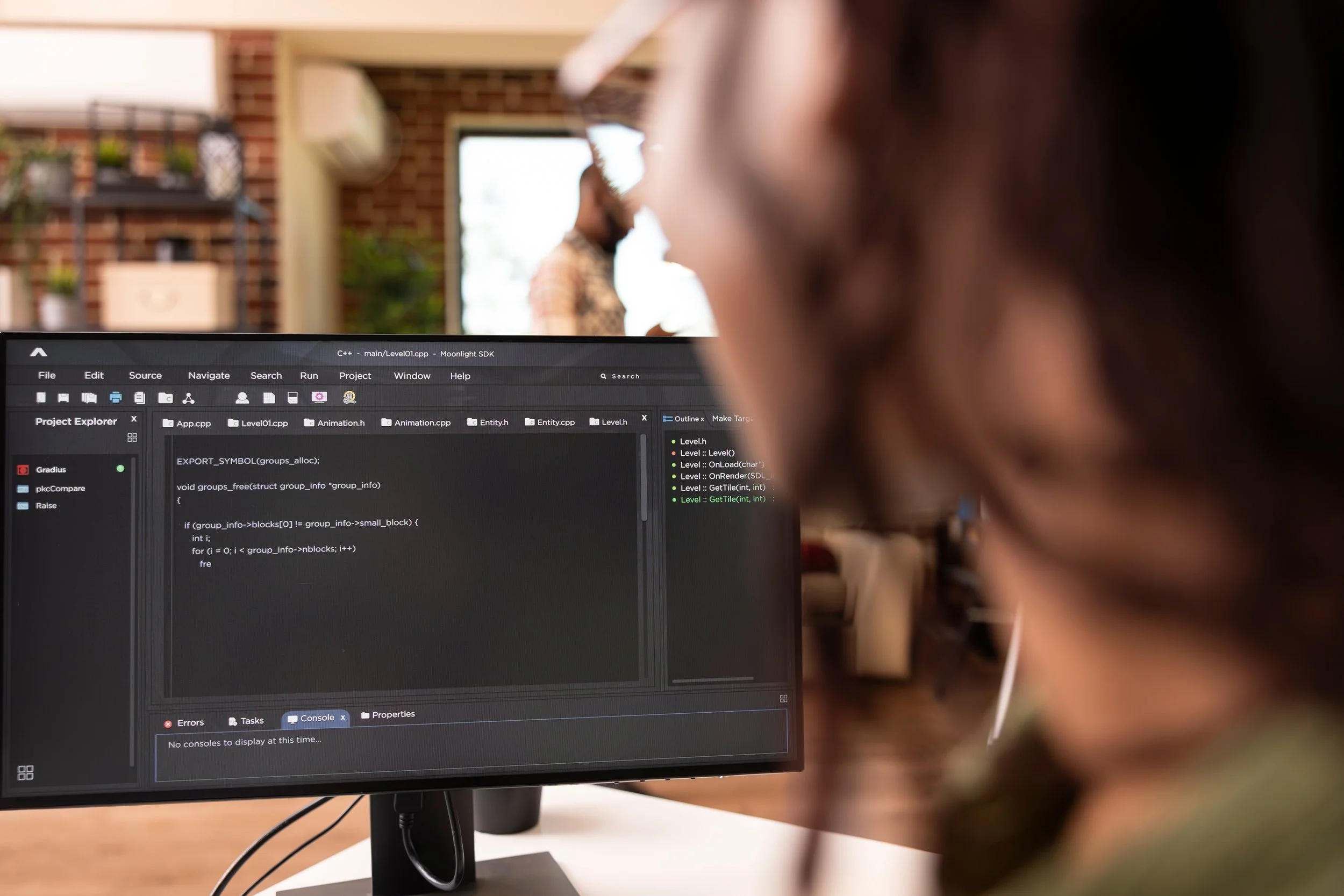 Person working on computer with C++ programming code visible on screen, in a modern office or coworking space.