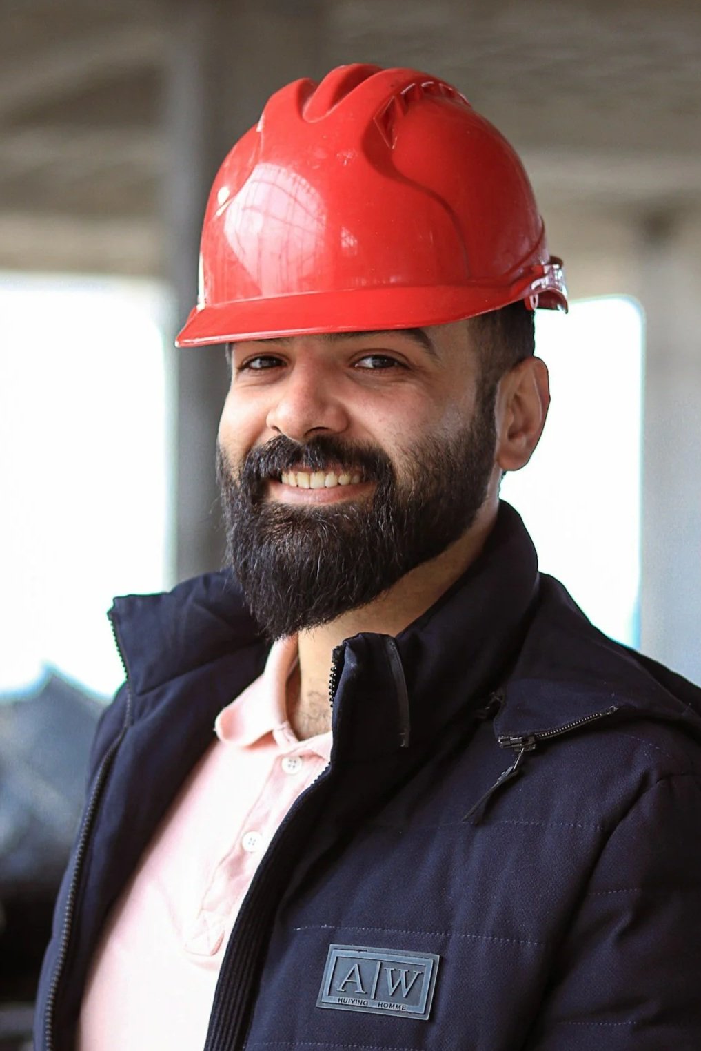 Close-up of a man with curly dark hair, clear glasses, light skin, wearing a dark sweater, smiling slightly, with a blurred background.