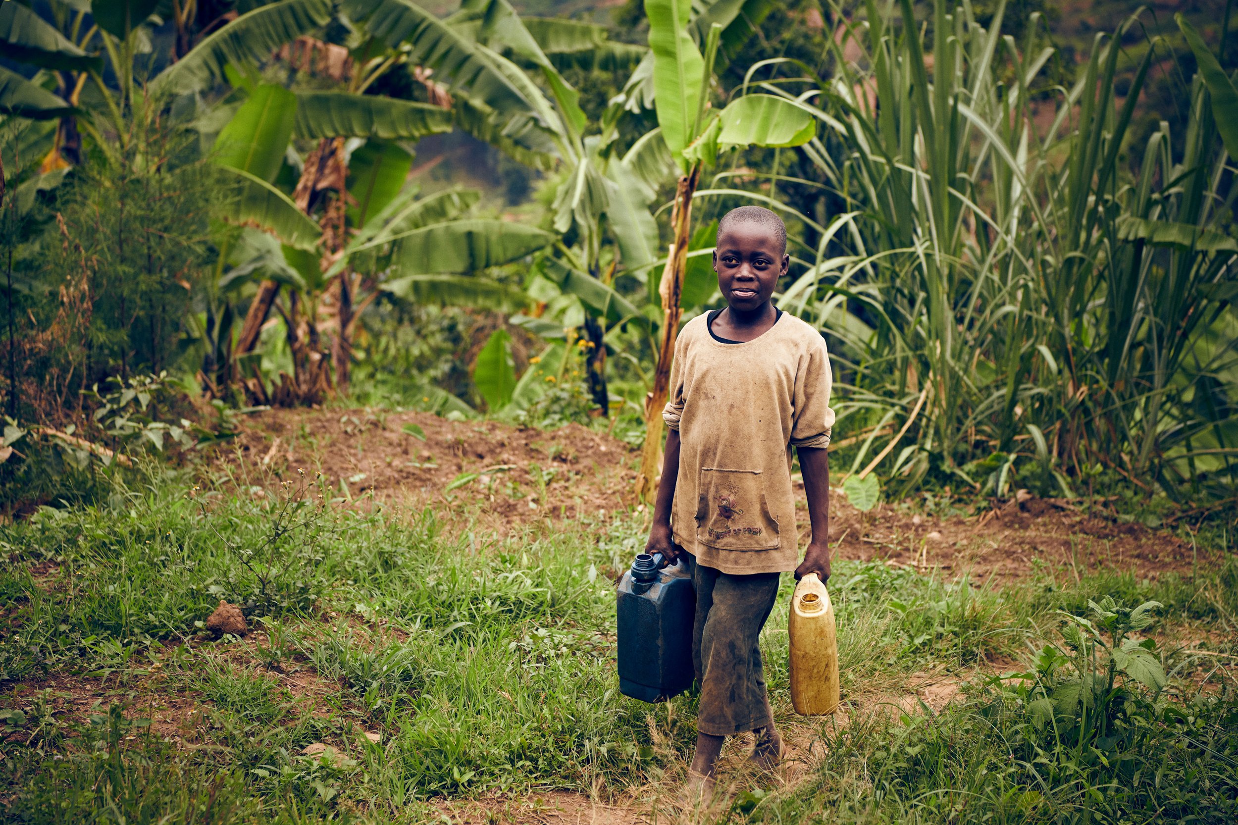 Child carrying water containers along path, everyday task in rural environment