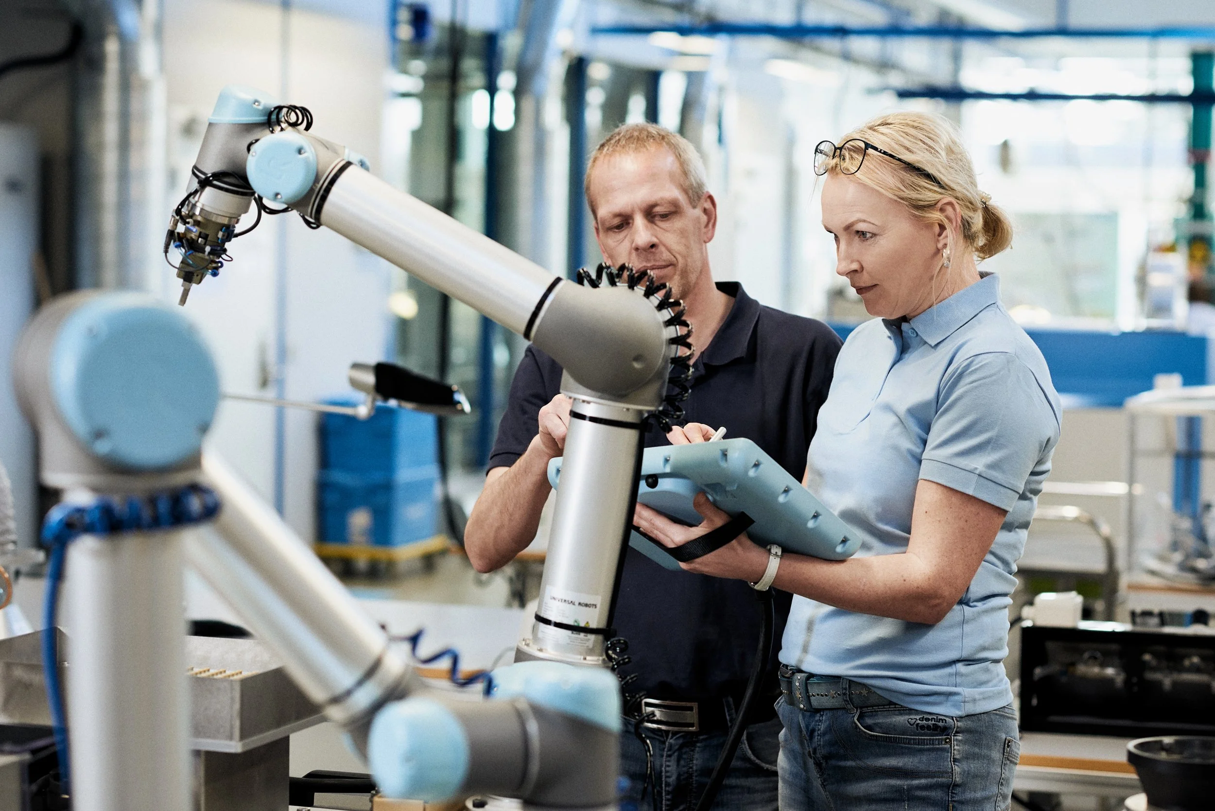 Two engineers programming collaborative robot using handheld controller in production setup