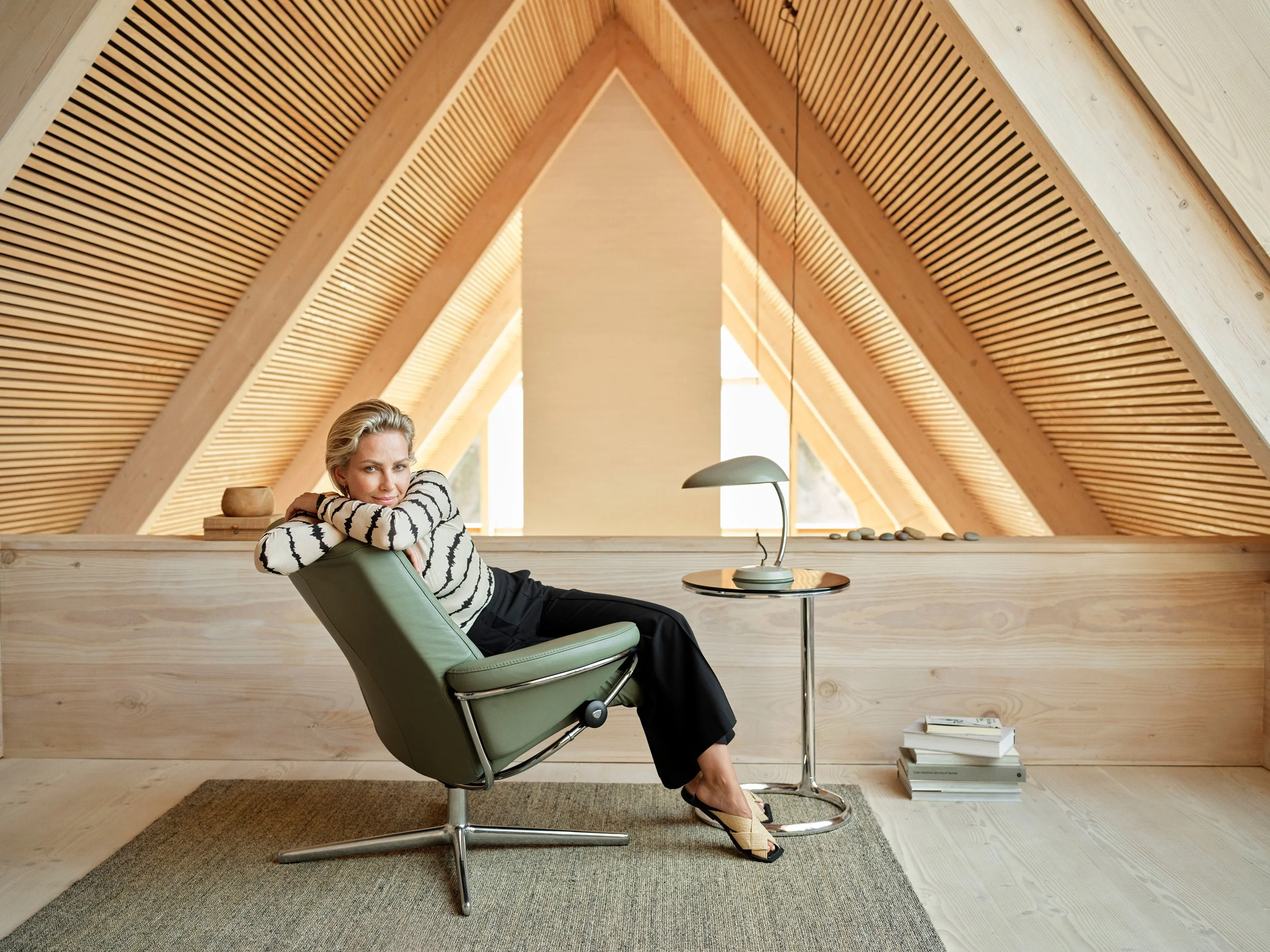 Woman reclining in chair in wooden attic interior, relaxed posture in natural light