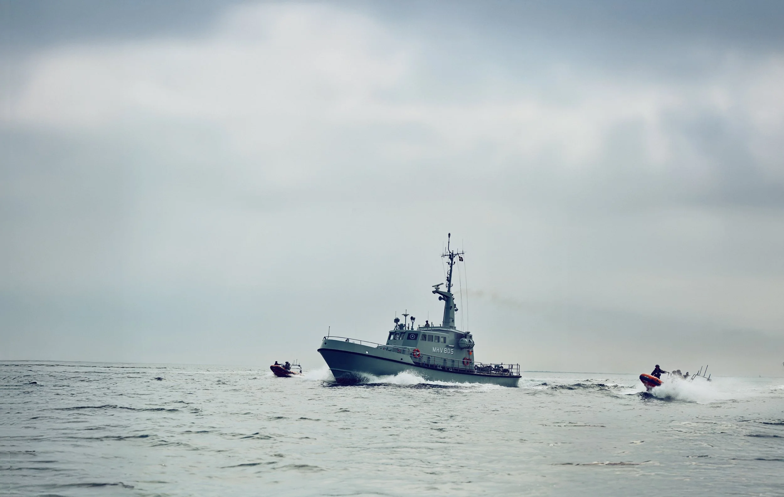 Naval Home Guard vessel sailing at sea with two smaller boats alongside under overcast sky
