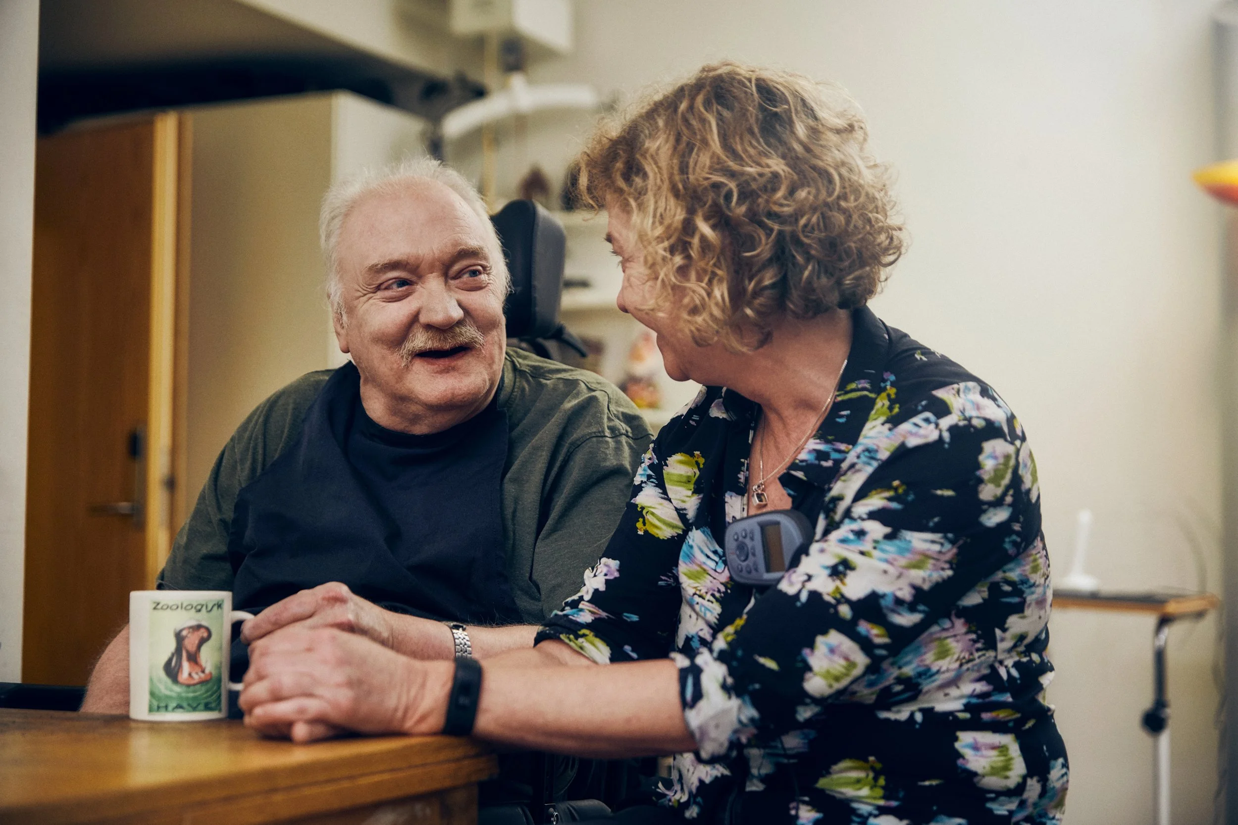 Elderly man and caregiver sitting together at table, conversation and support situation