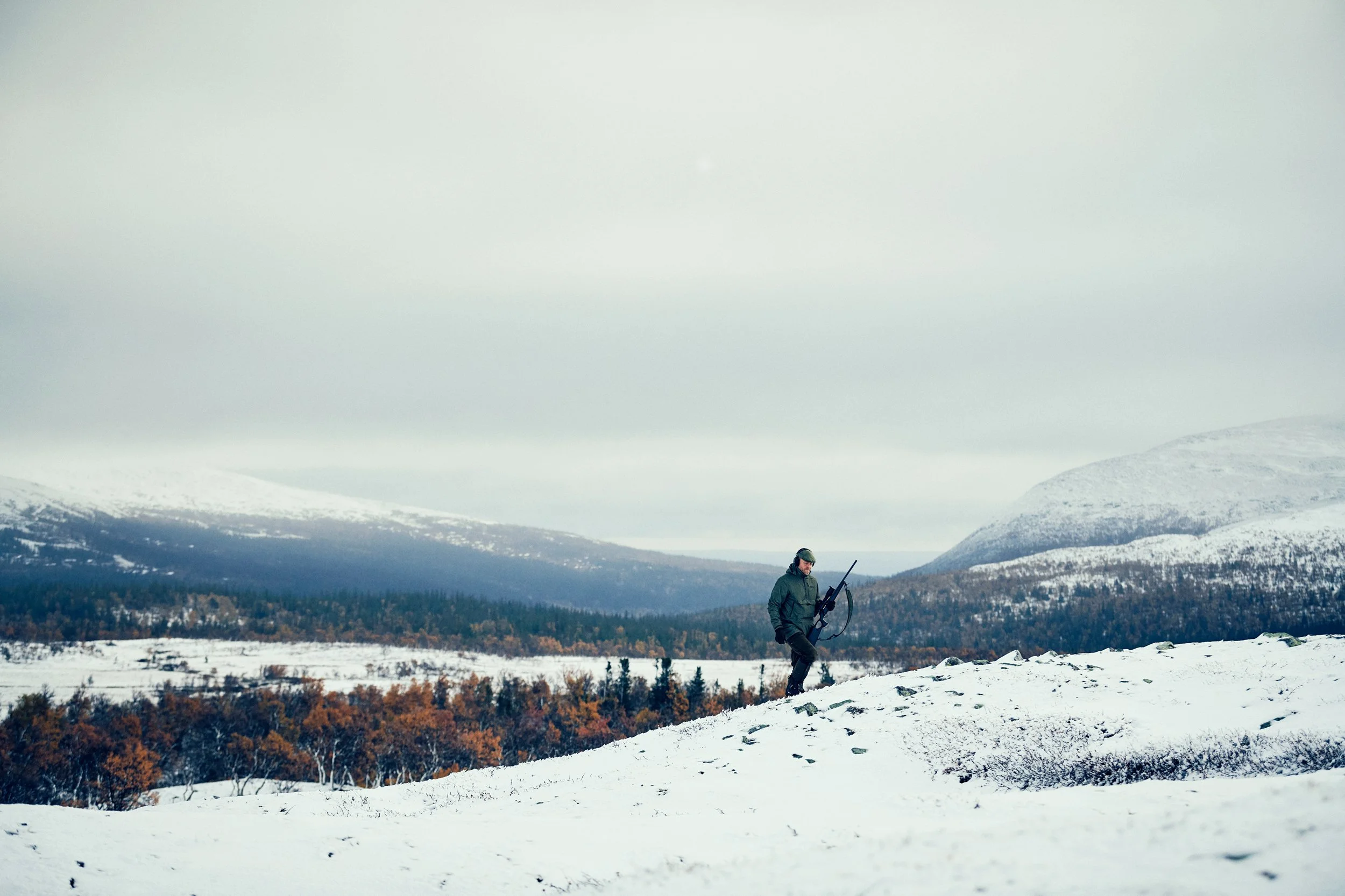 Hunter standing alone in snowy landscape, scale and distance in mountainous terrain