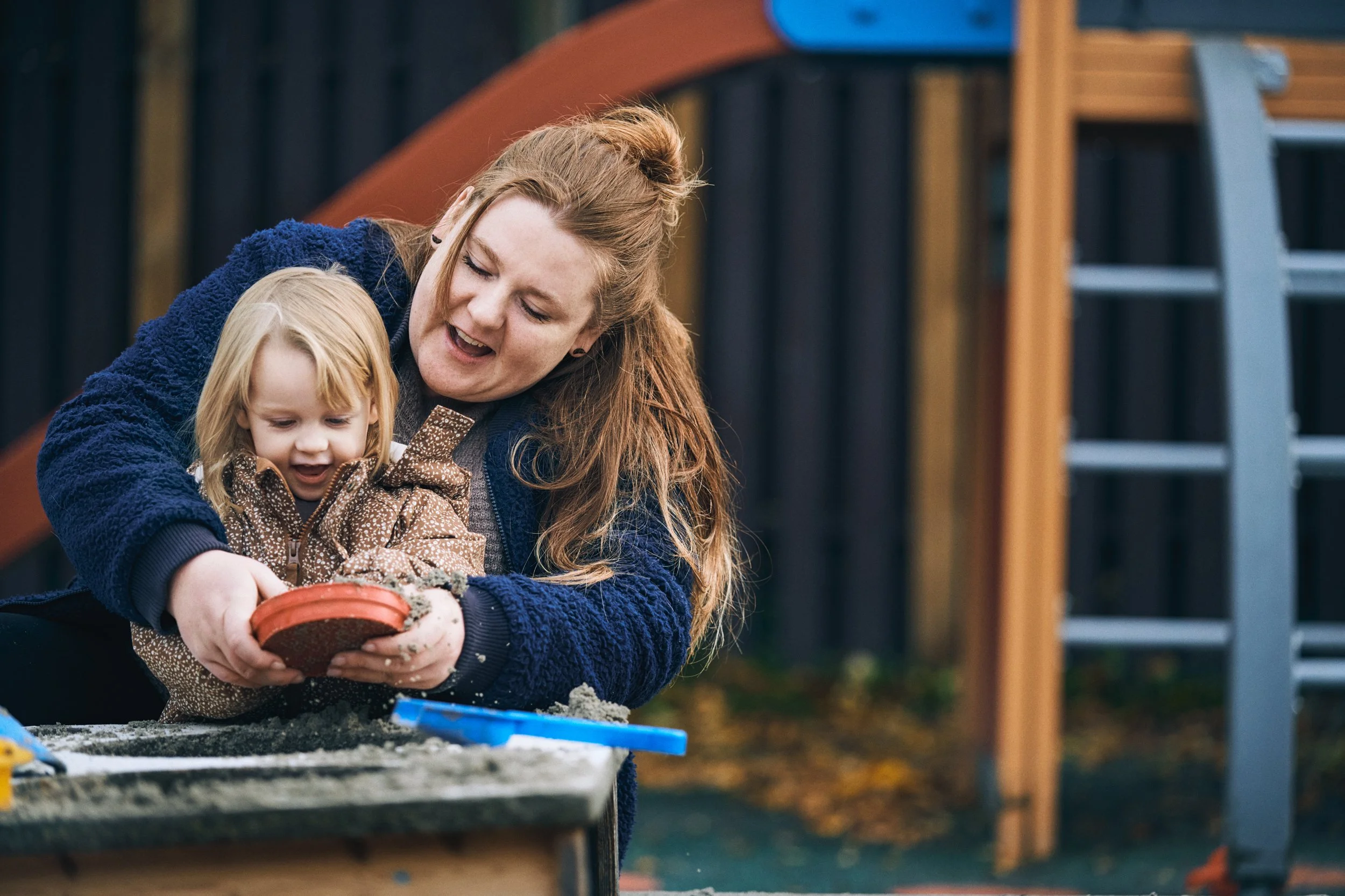 Adult and child playing with sand at playground, shared moment in childcare setting