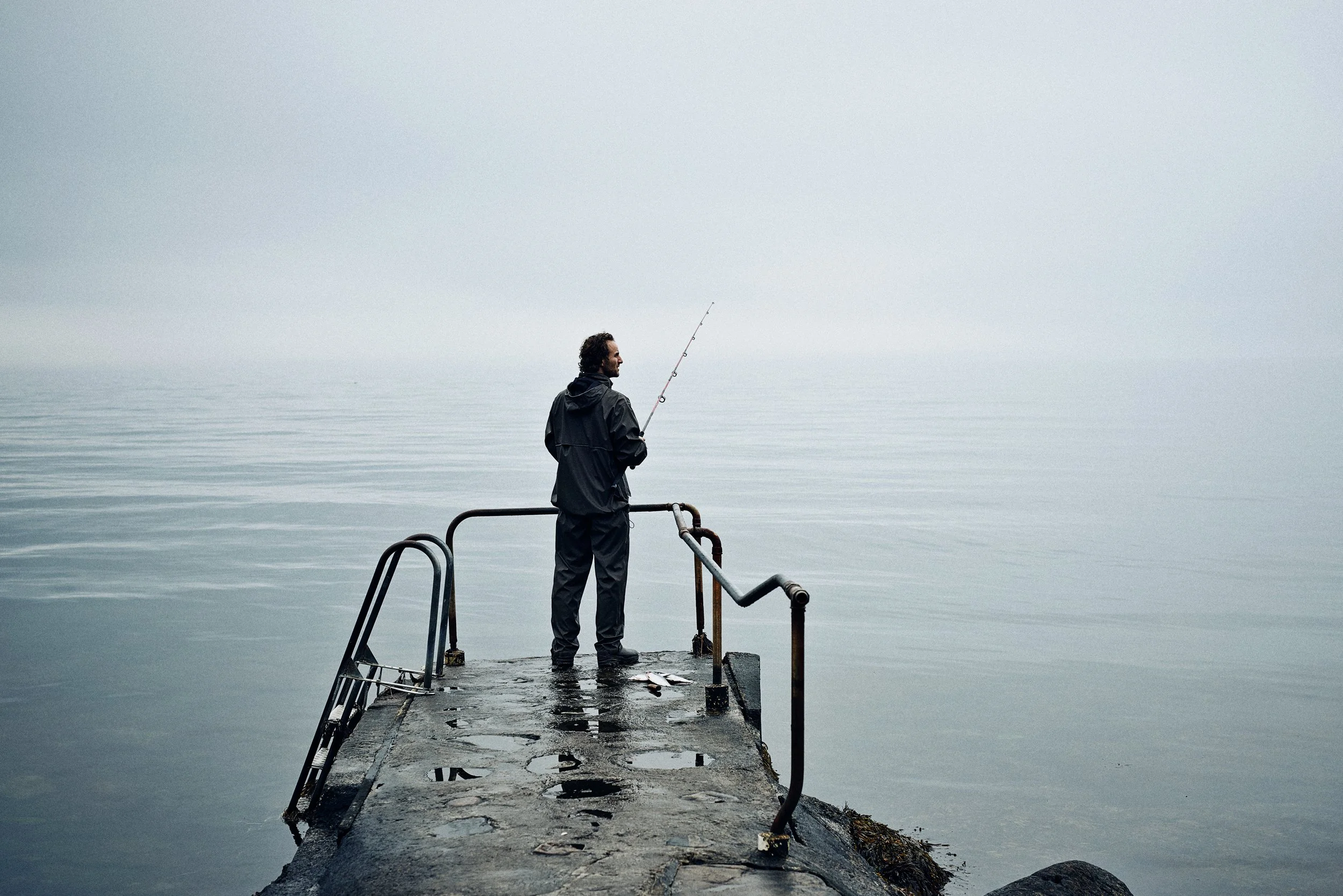 01
Man fishing from concrete pier in calm sea, solitary moment in foggy coastal setting