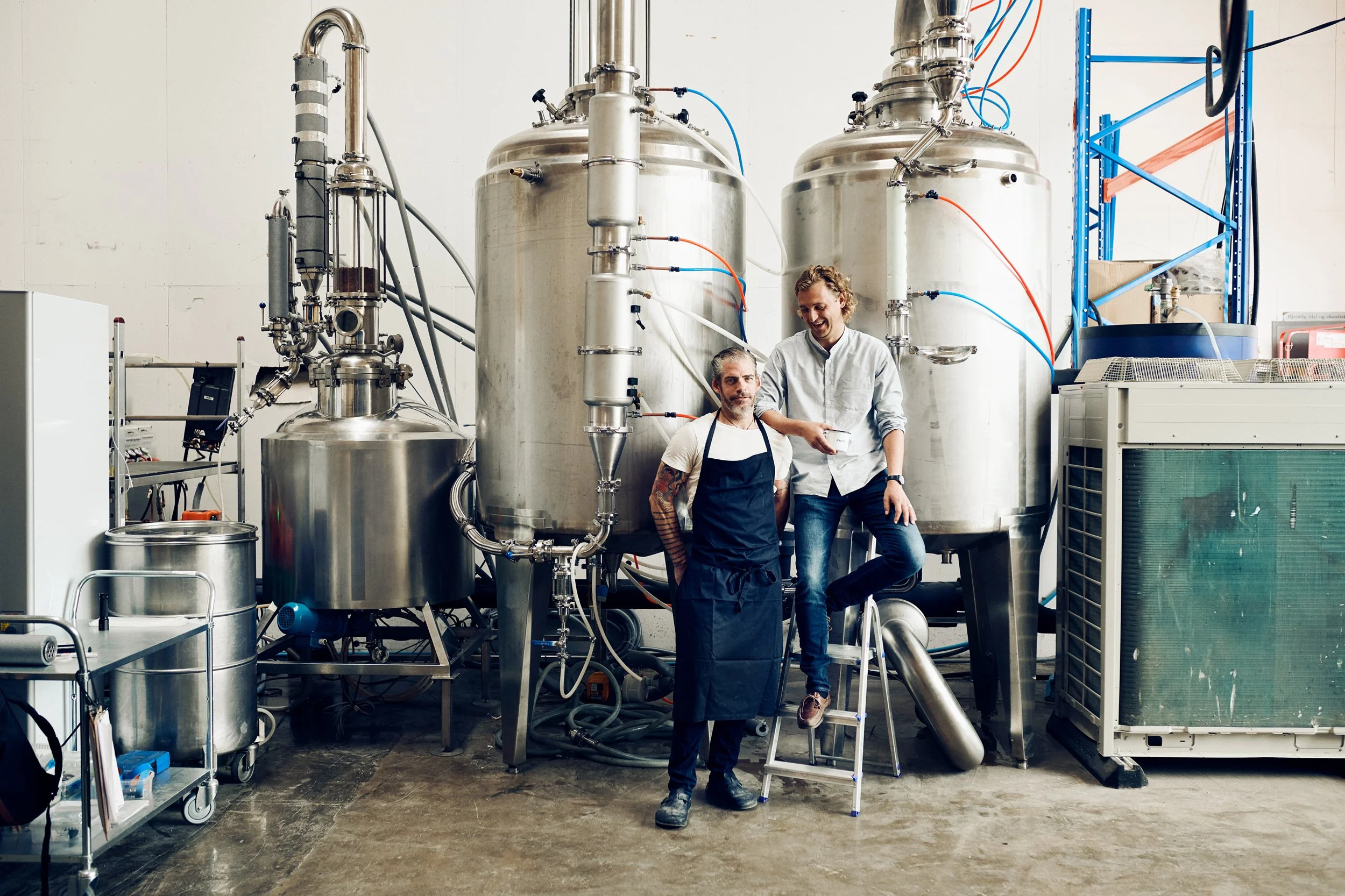 Two people standing in distillery among large tanks, production environment overview