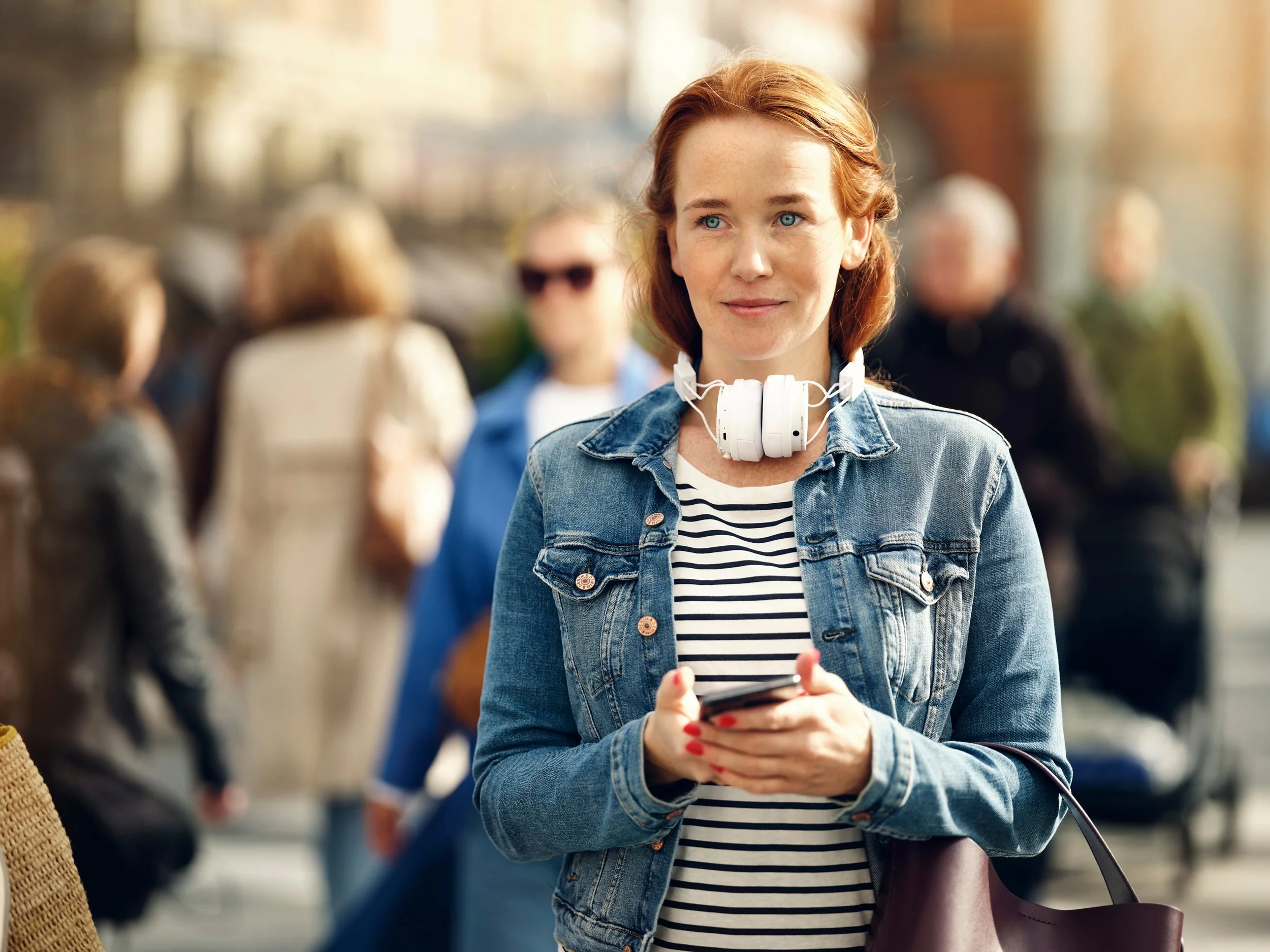 Woman walking in city holding phone in her hands, active urban lifestyle