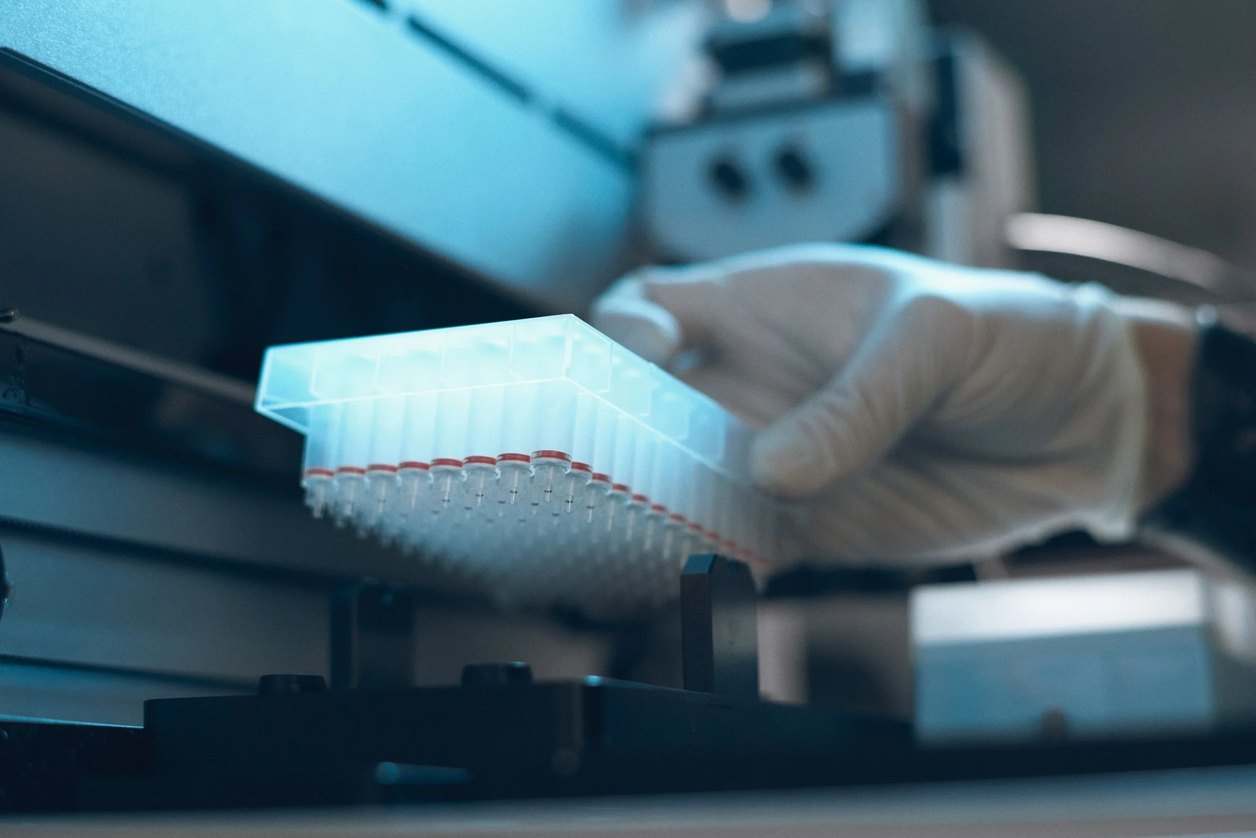 Gloved hand placing multi-well sample plate into automated analysis system for laboratory testing